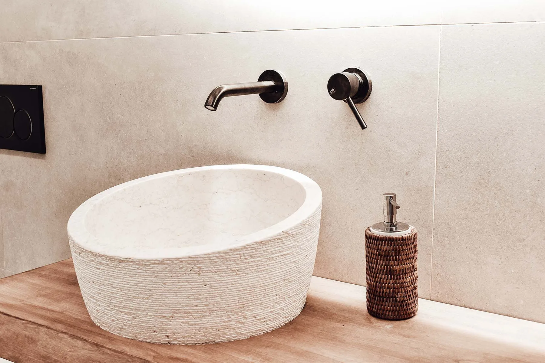 A bathroom sink sits on a wooden vanity beneath a wall-mounted faucet.