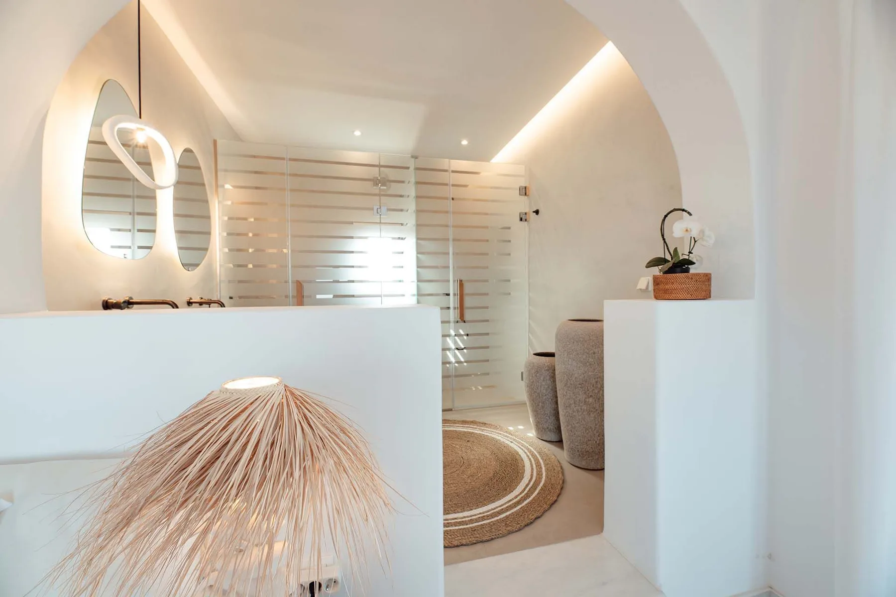 A bright bathroom with a glass shower and round woven rug.