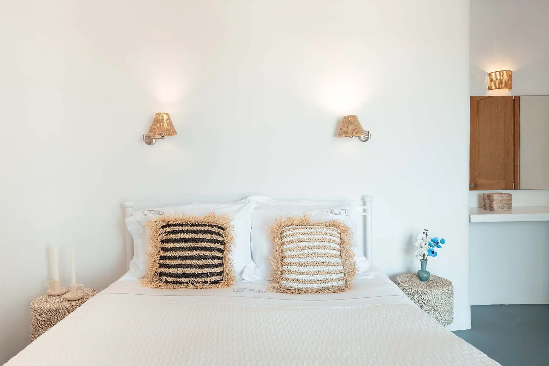 A bright bedroom with a bed dressed in white and two striped pillows.