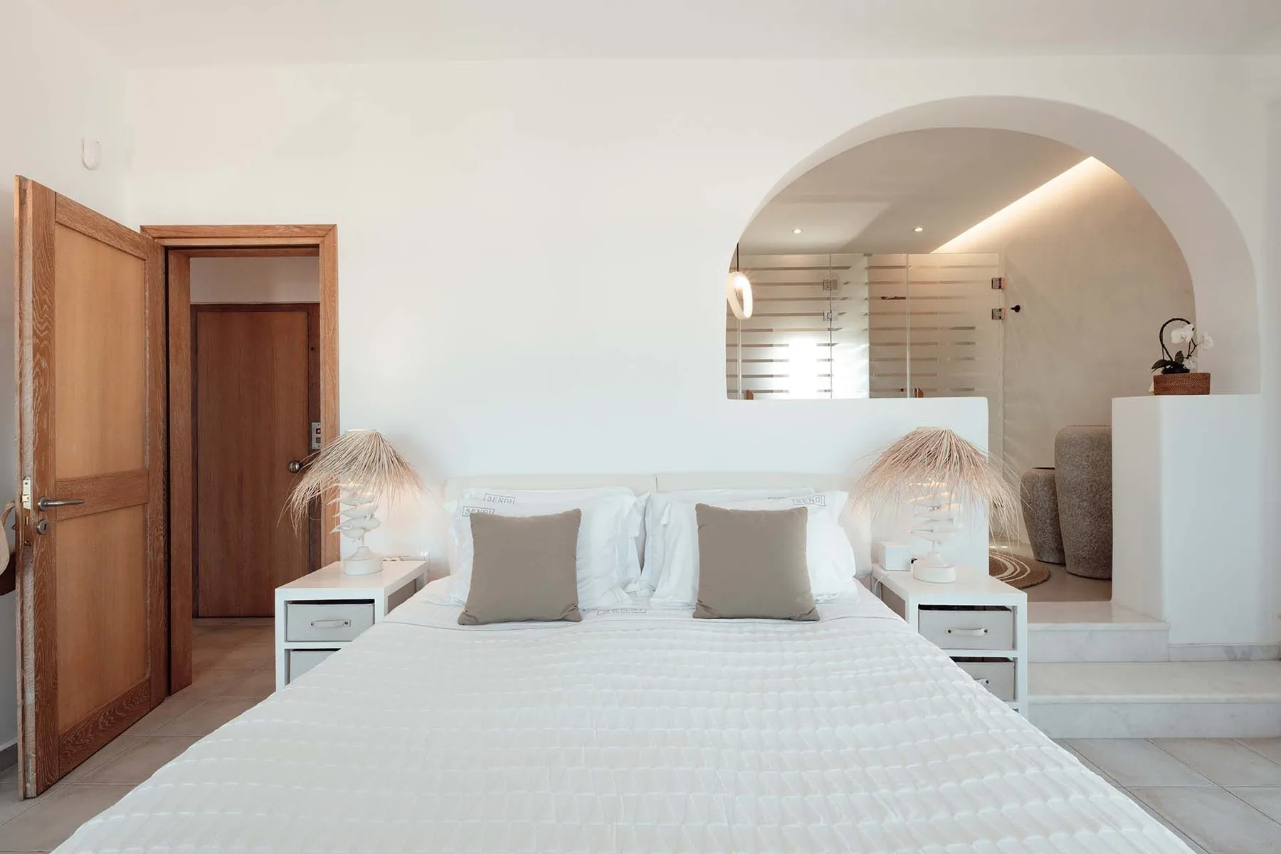A bedroom with a neatly made bed and an arched opening to an adjoining area.