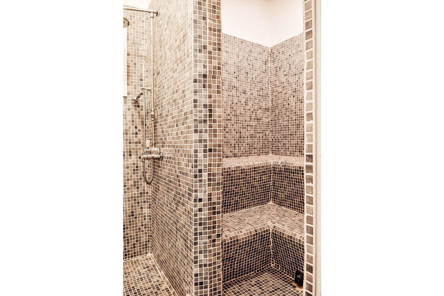 A tiled shower area with a handheld showerhead and built-in seating.