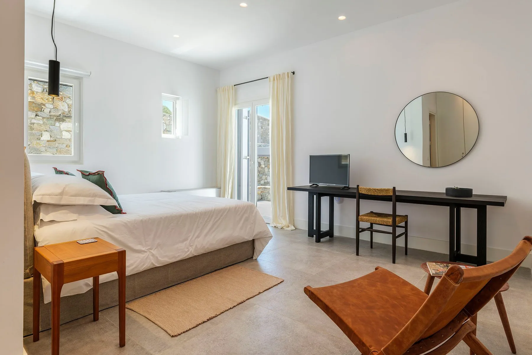 A bedroom with a bed, a desk, and a round wall mirror.