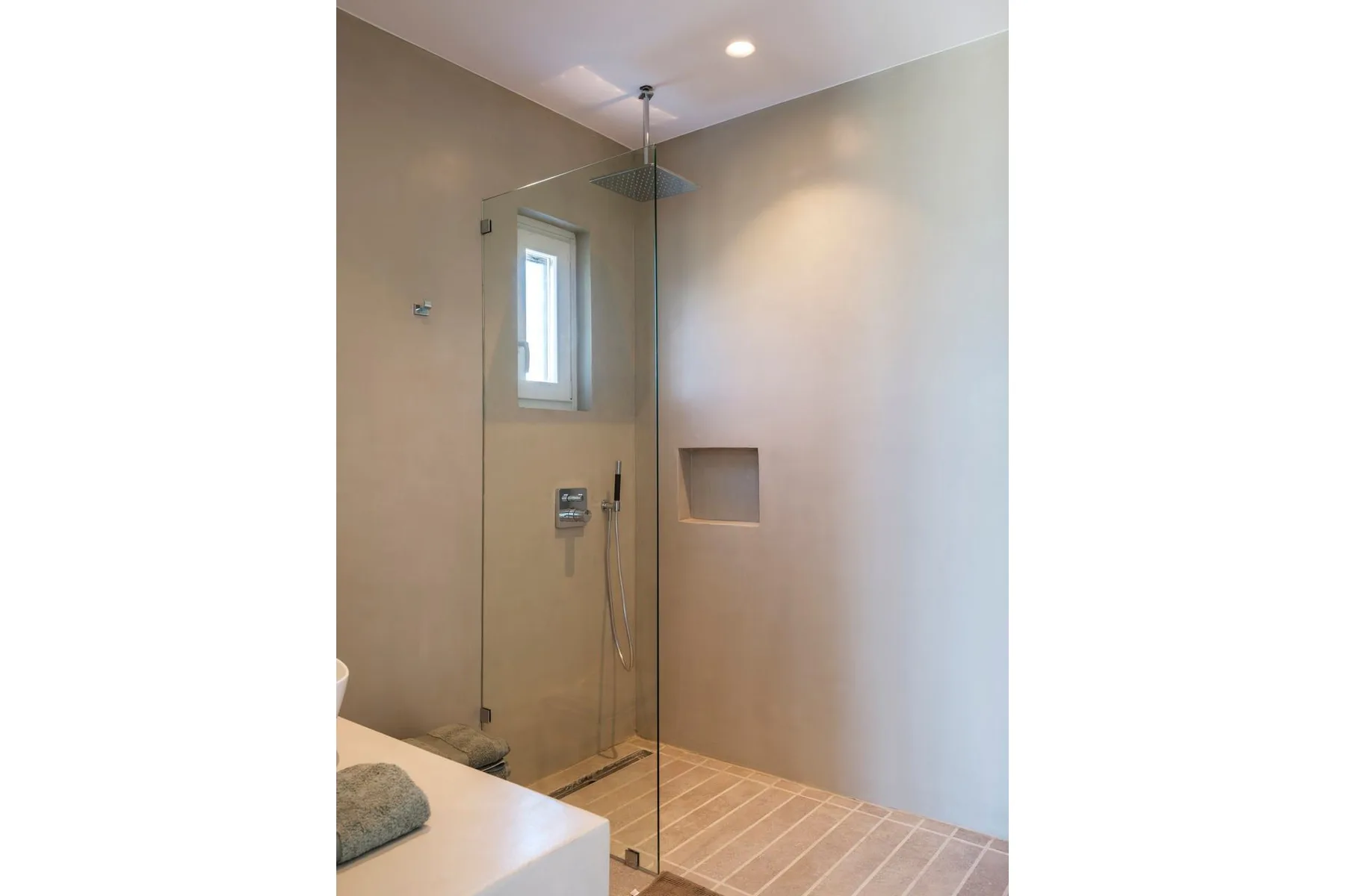 A tiled shower with a glass panel and a small window.