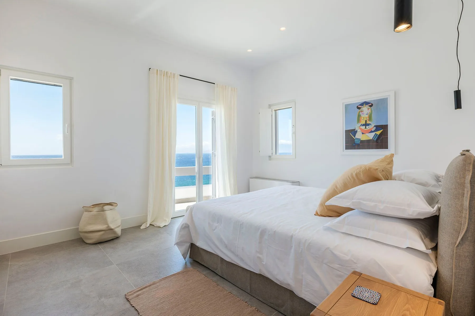 A bright bedroom with a bed beside tall windows overlooking the water.