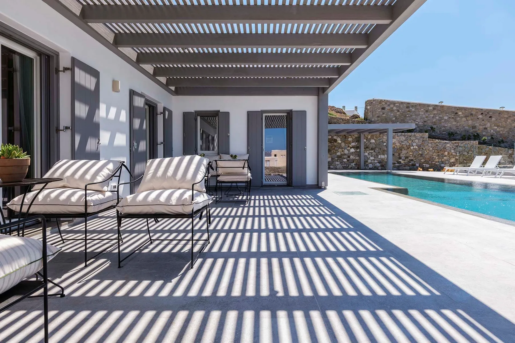 A shaded outdoor patio with lounge seating beside a swimming pool.