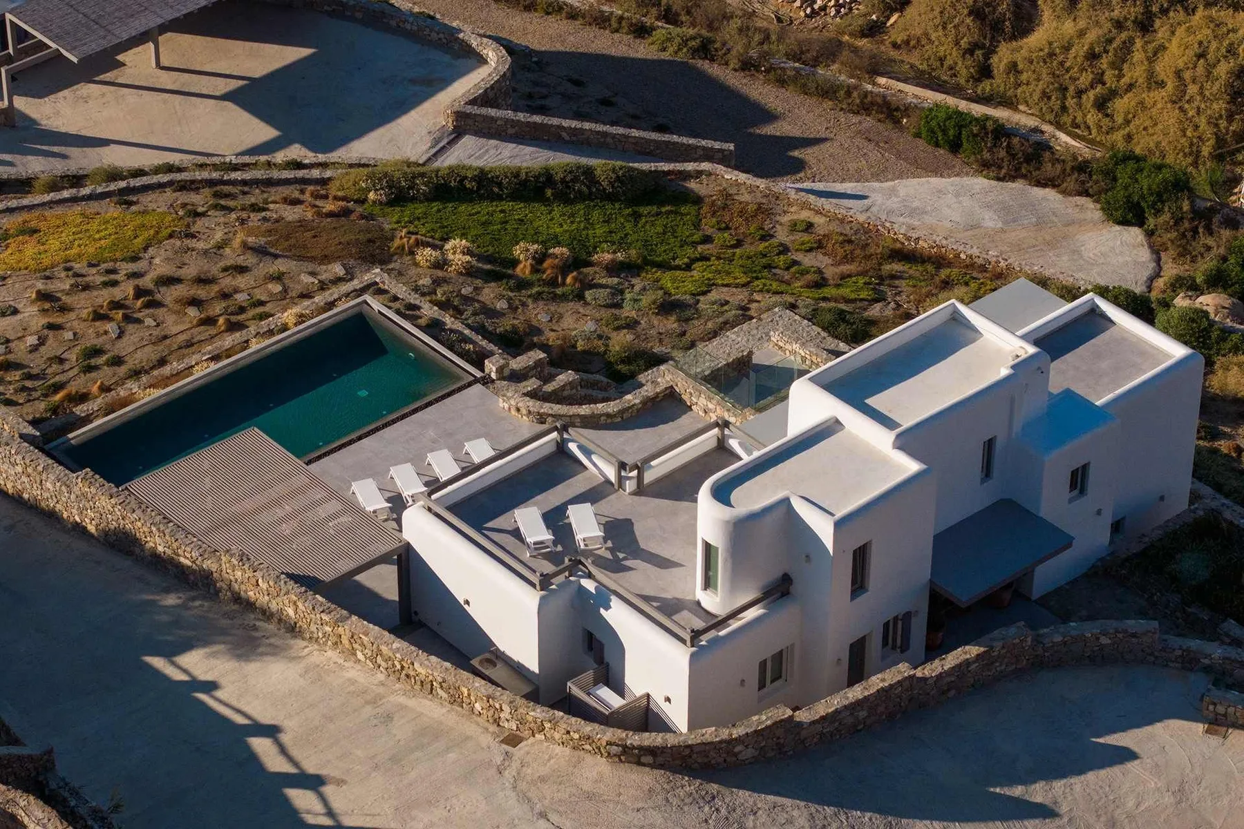 Aerial view of a white house beside a rectangular swimming pool and outdoor seating.