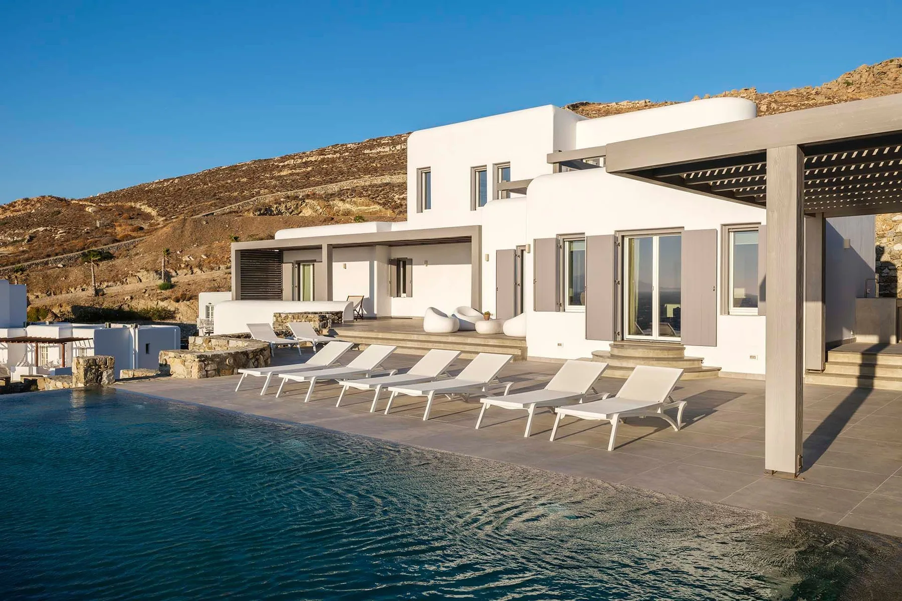 A modern white villa opens onto a terrace with a swimming pool and lounge seating.