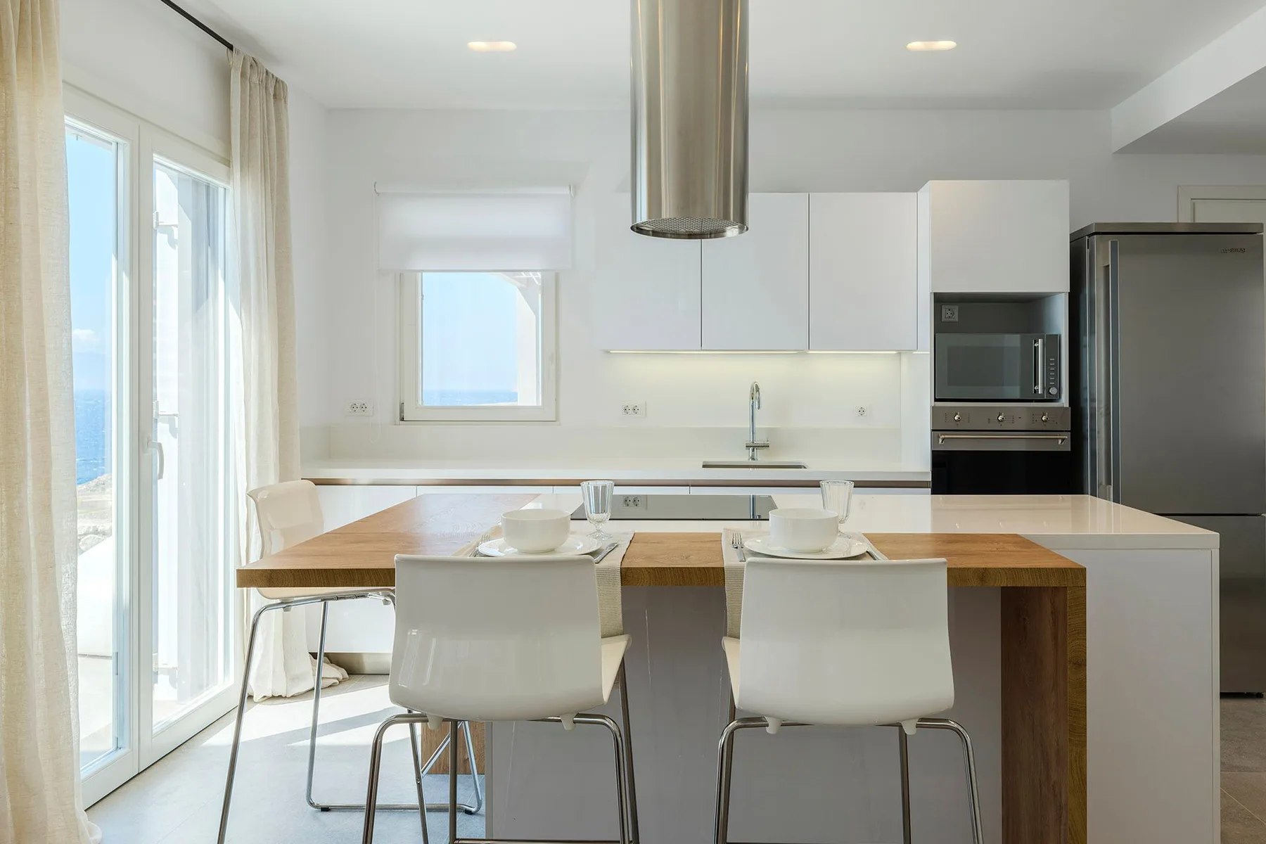A bright modern kitchen with a central island and dining chairs.