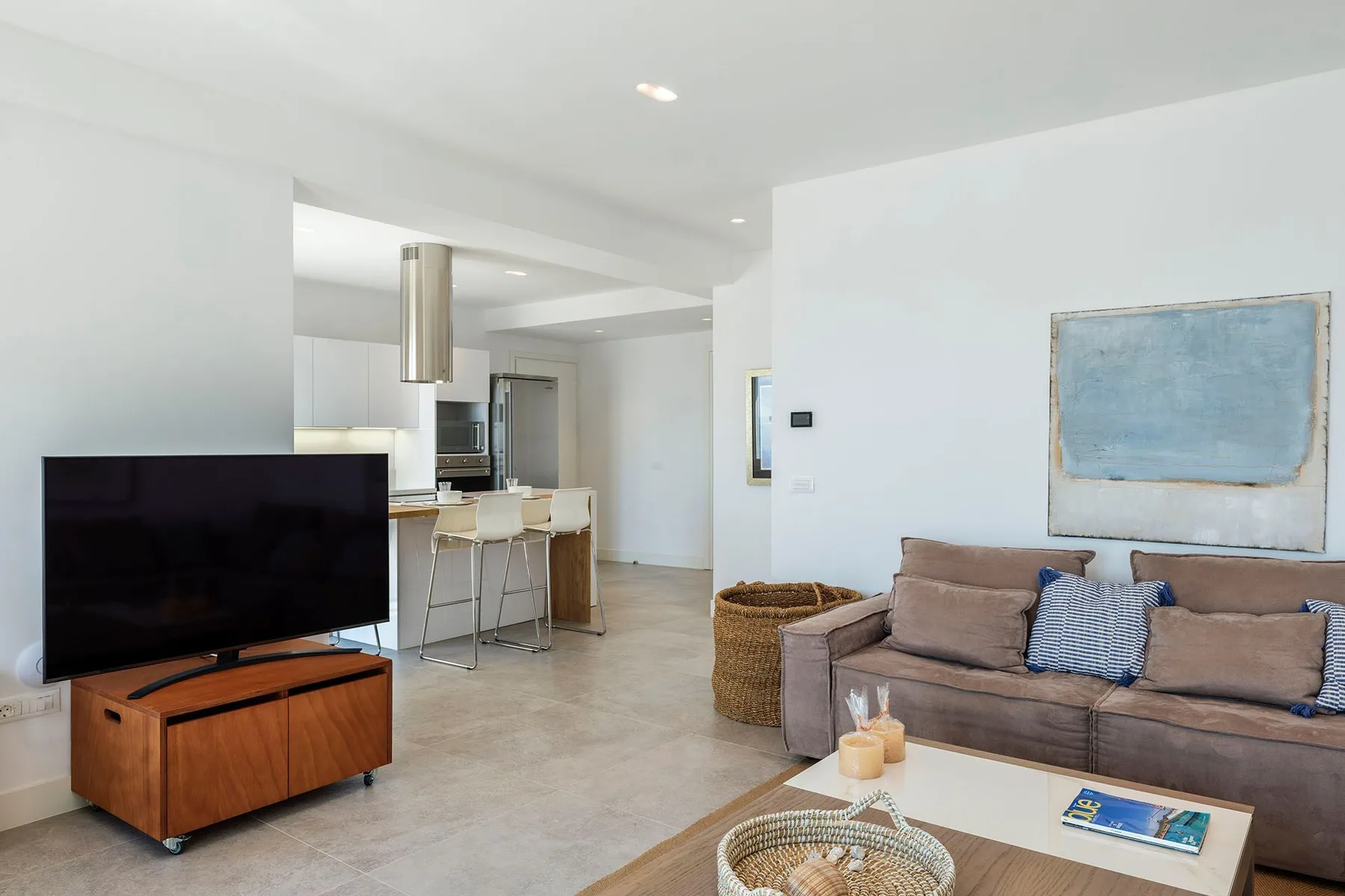 A bright living room with a television, seating, and an open kitchen.