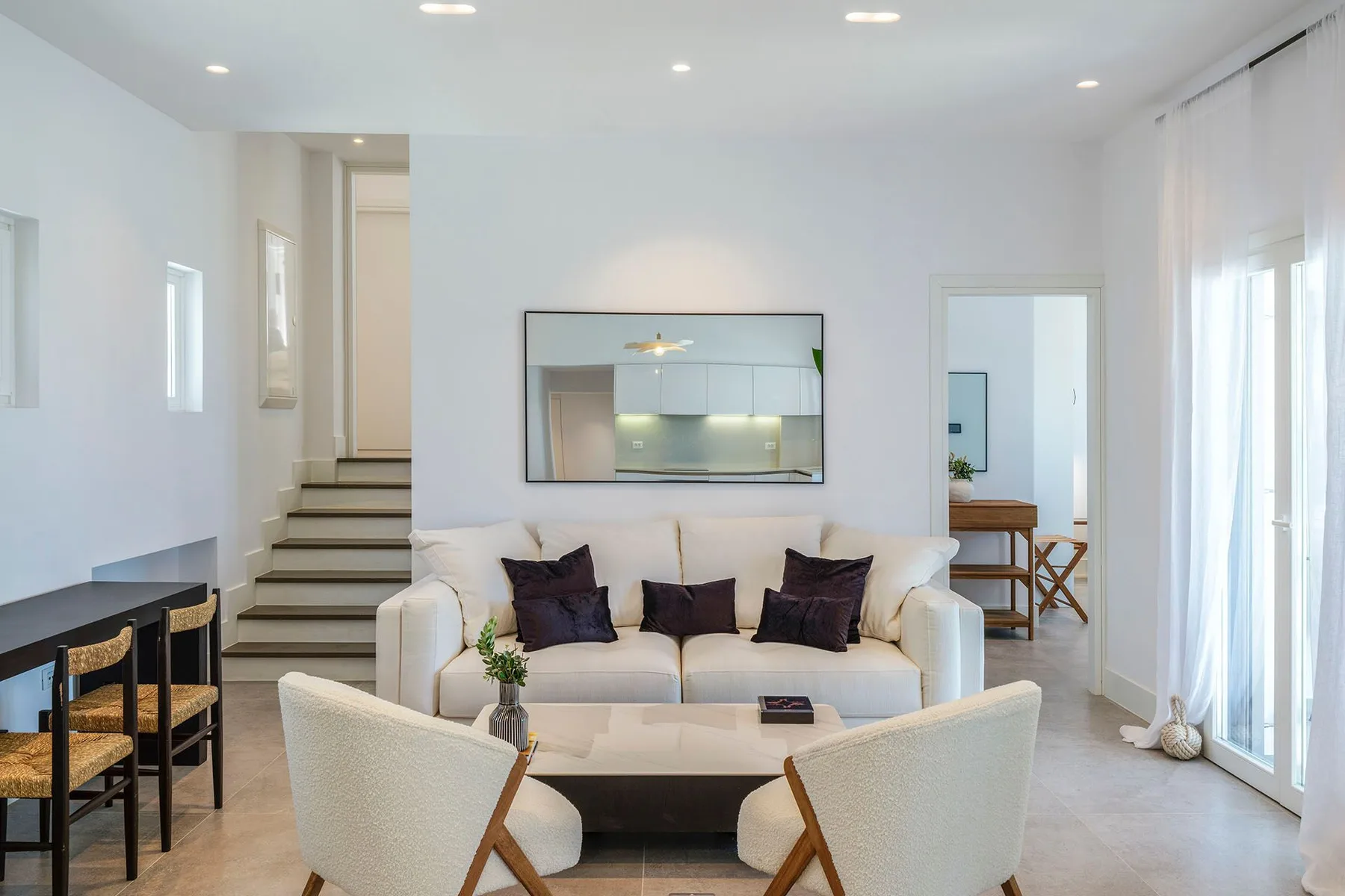 A bright living room with a sofa, two chairs, and a wall mirror.