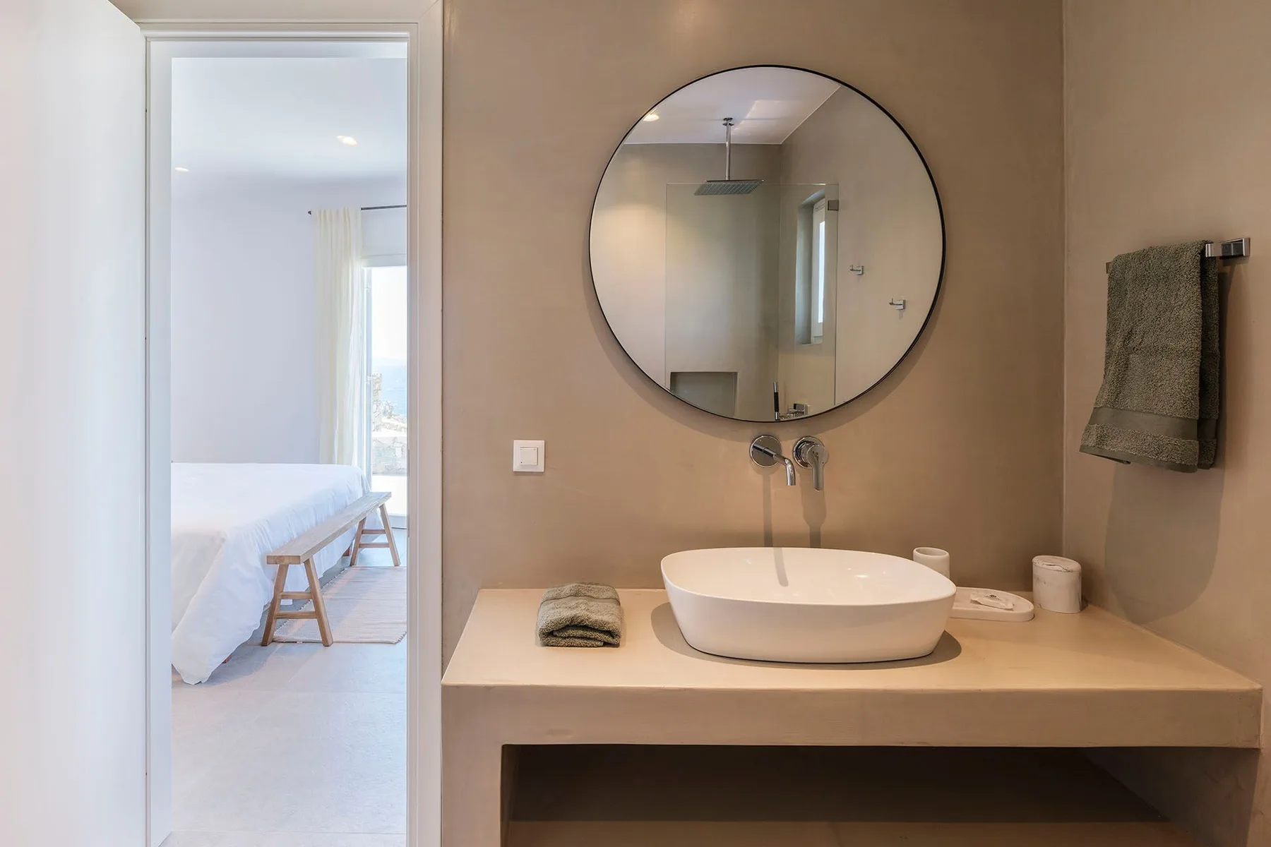 A bathroom vanity with a vessel sink and round mirror, beside an open doorway.