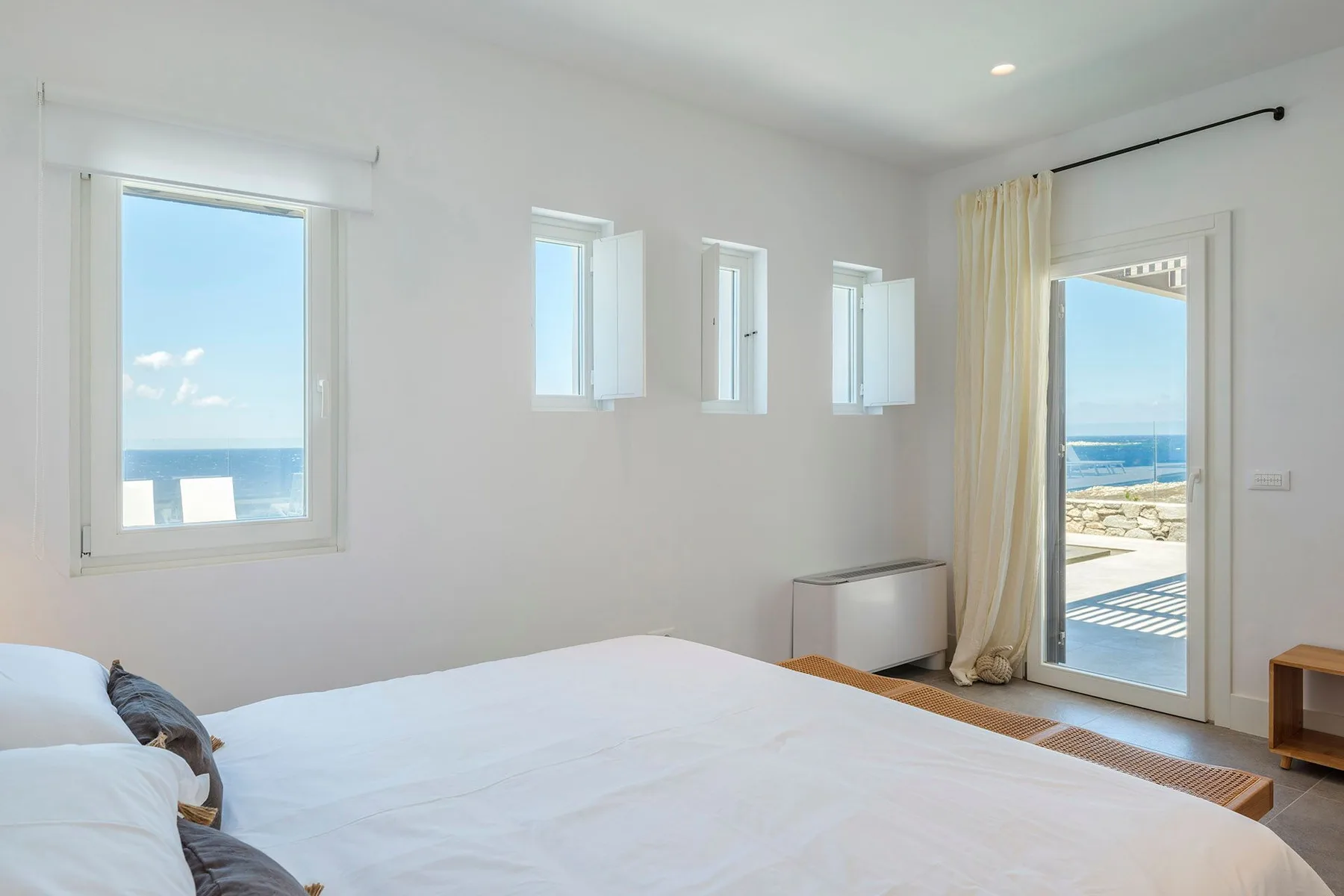 A bright bedroom with a bed and windows overlooking the sea.