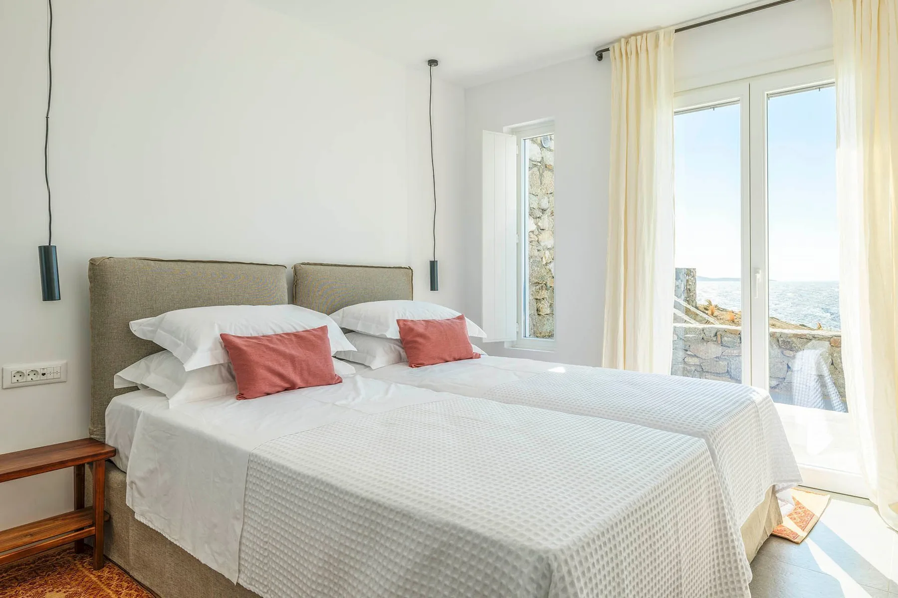 A bright bedroom with two beds beside large glass doors.