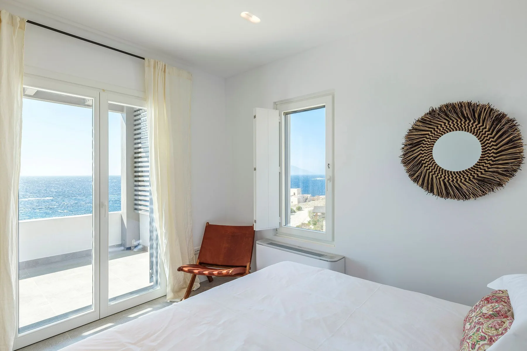 A bright bedroom with a bed, glass doors, and a view of the sea.