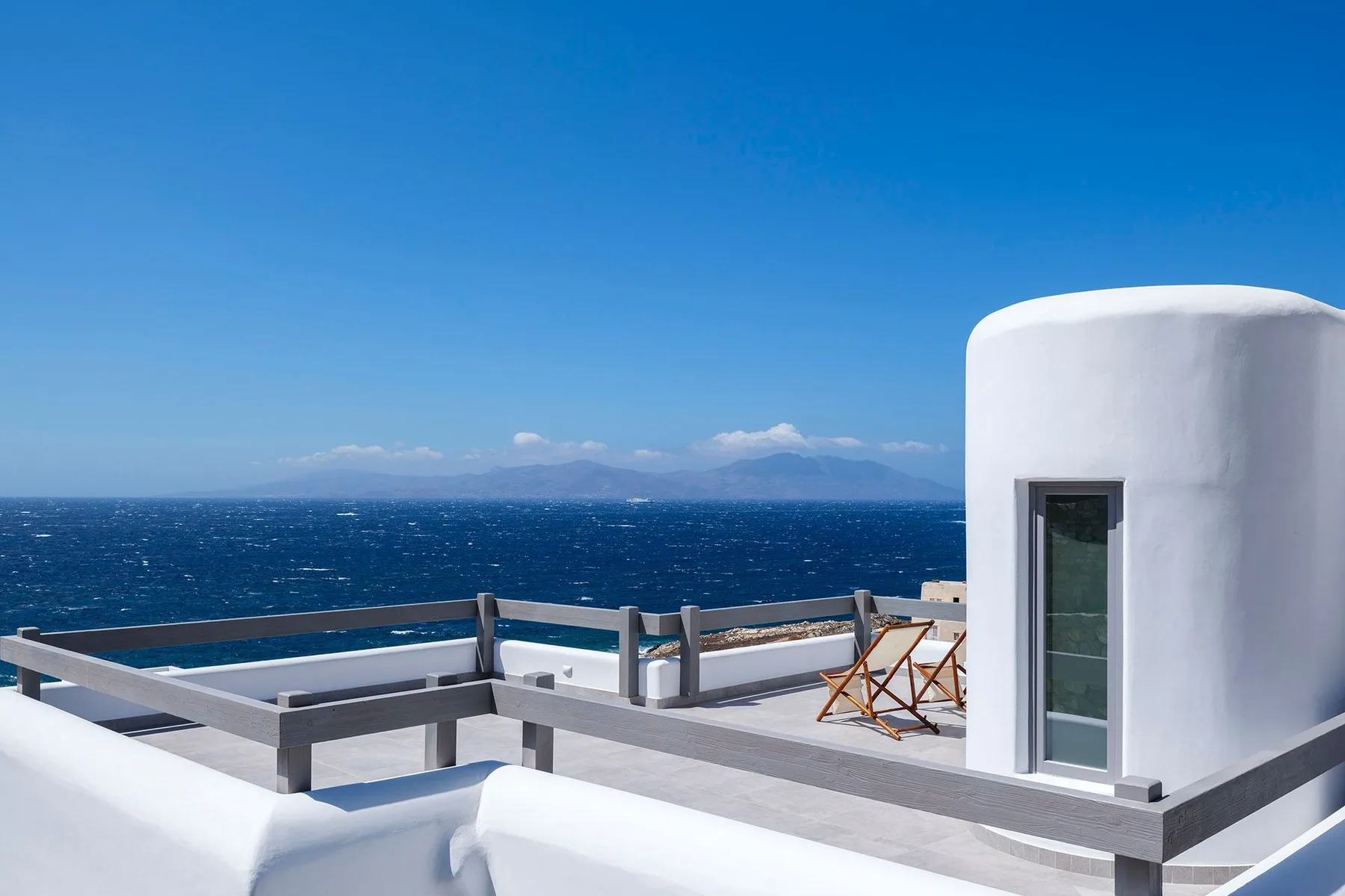 A seaside terrace overlooks the blue sea, with a small seating area.