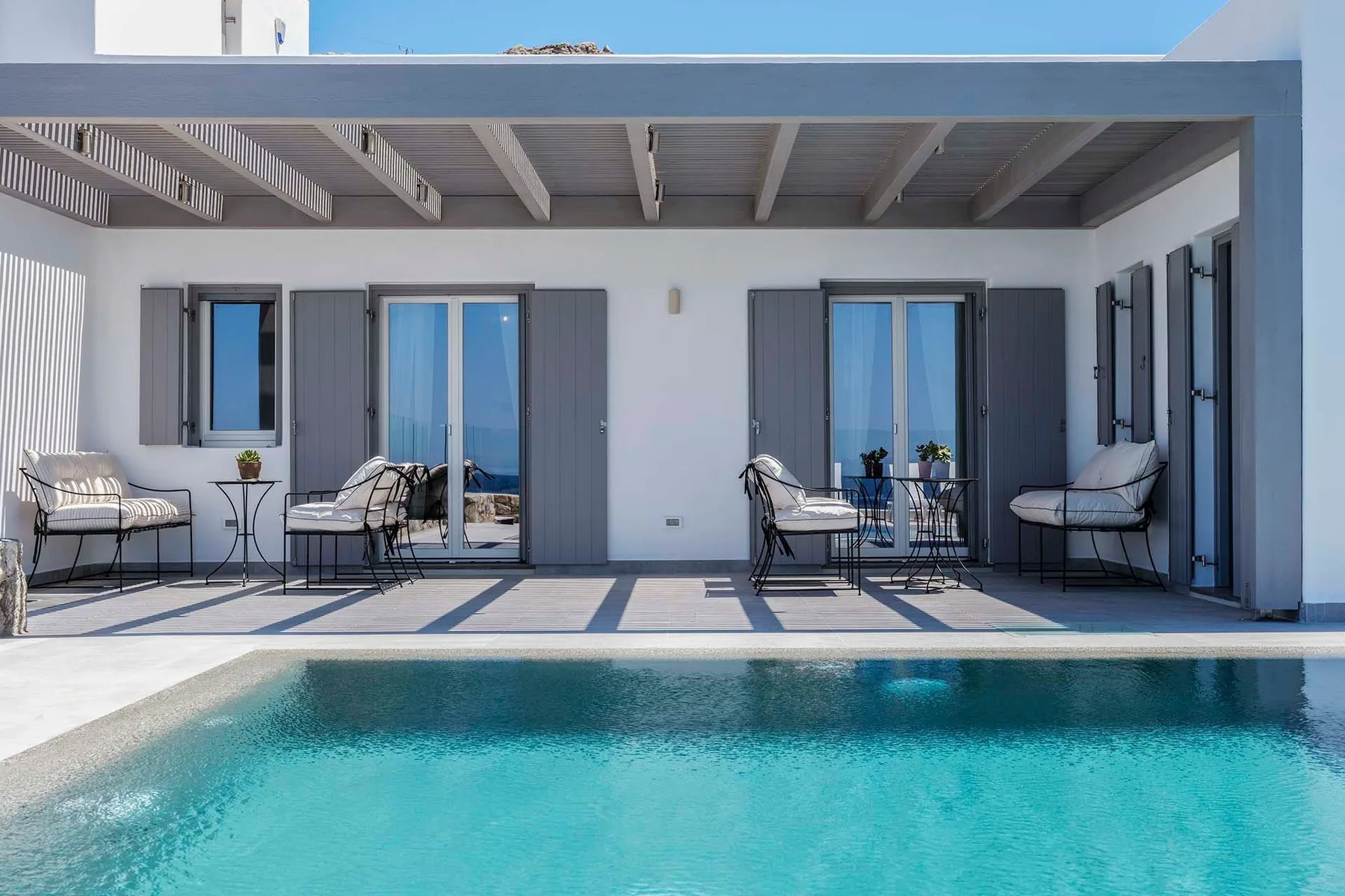A covered patio with seating overlooks a swimming pool.