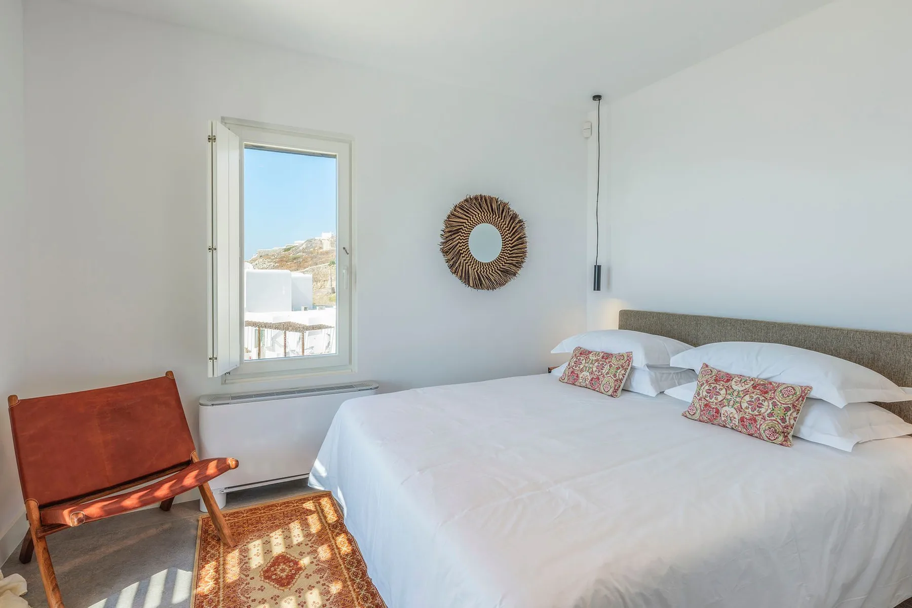 A bright bedroom with a bed, a window, and a wooden chair.