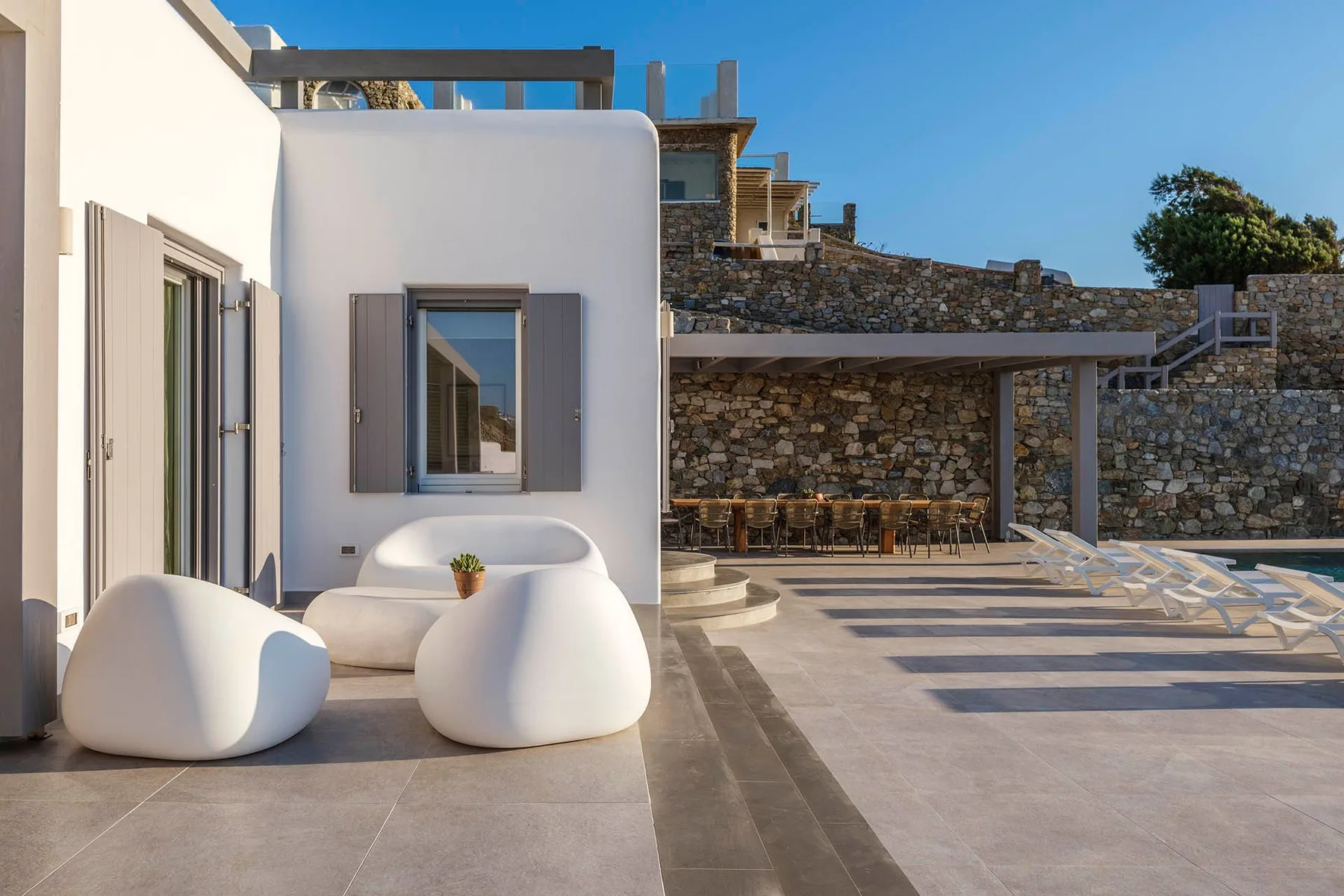 A sunny outdoor patio with sculptural seating beside a stone wall and pool.