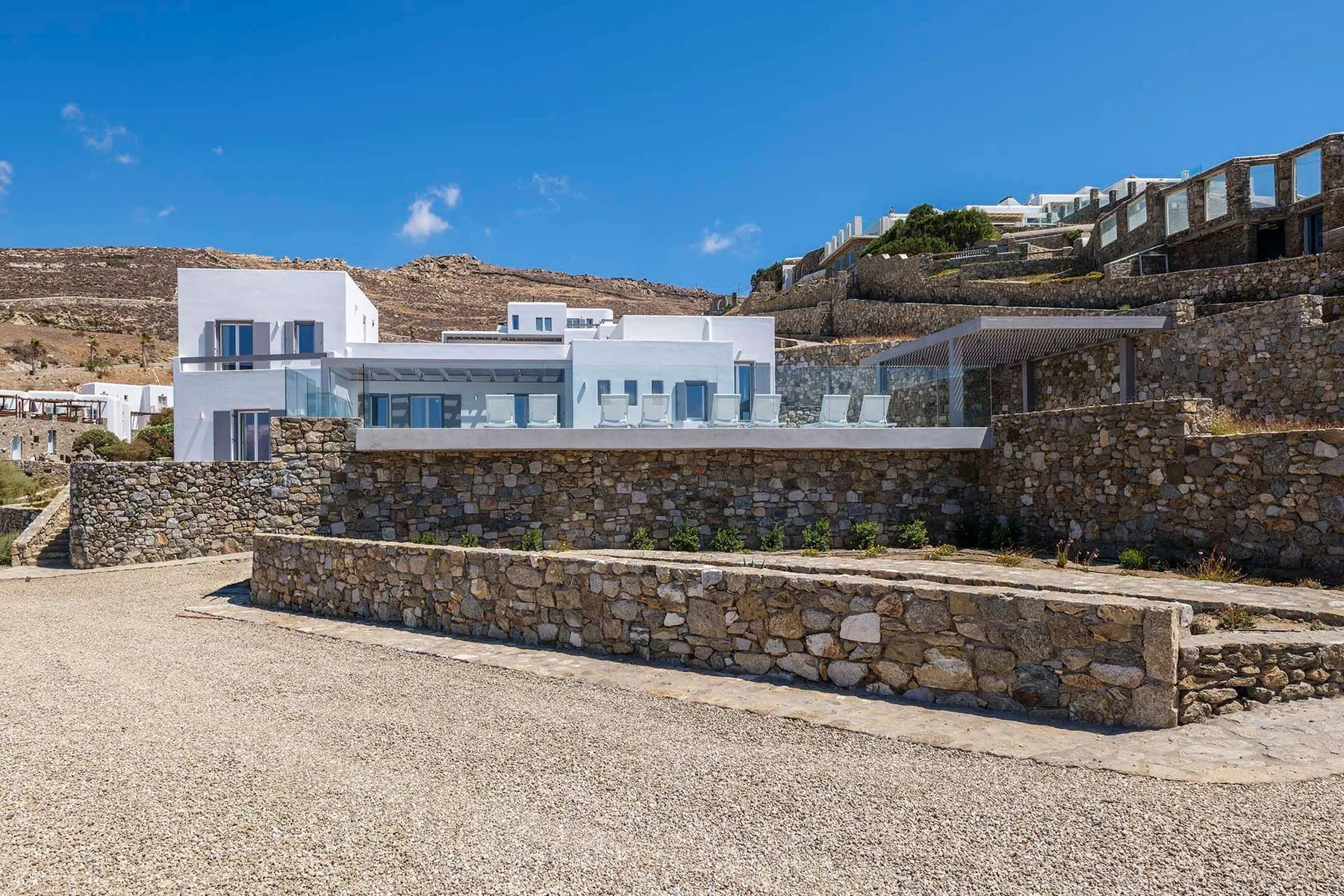 A modern white building sits behind stone retaining walls on a hillside.