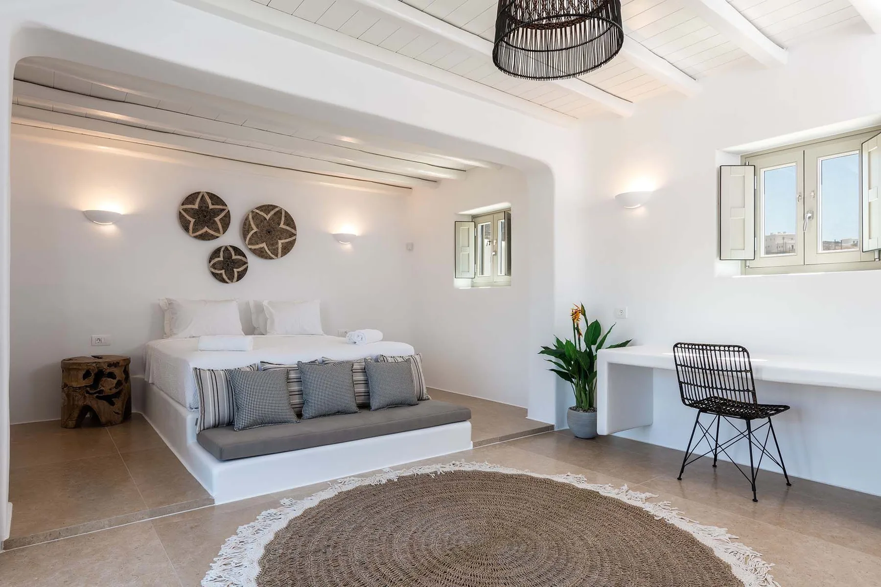 A bright bedroom with a low bed, woven rug, and windows along the wall.