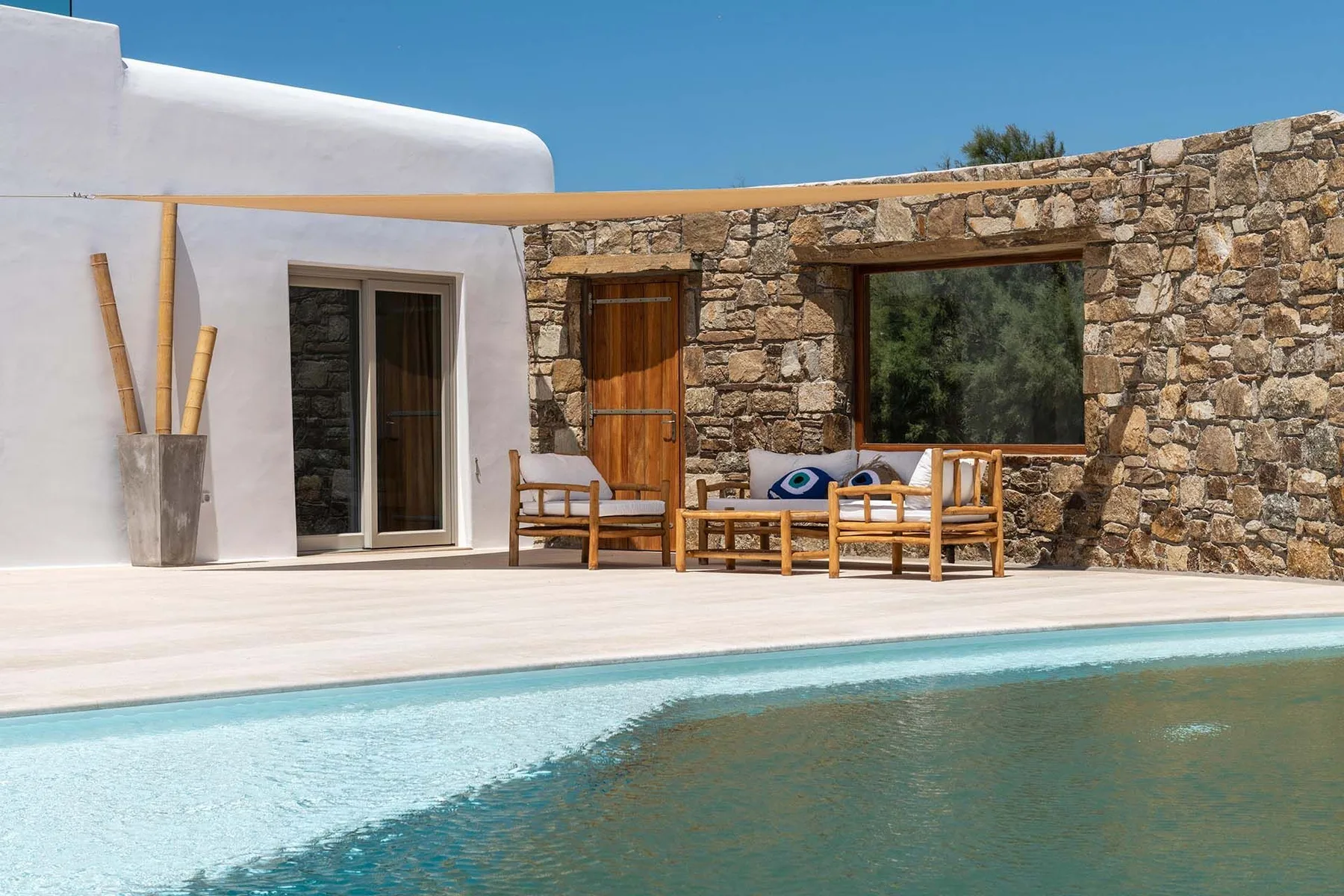 A poolside terrace has wooden seating beside a stone wall and white building.