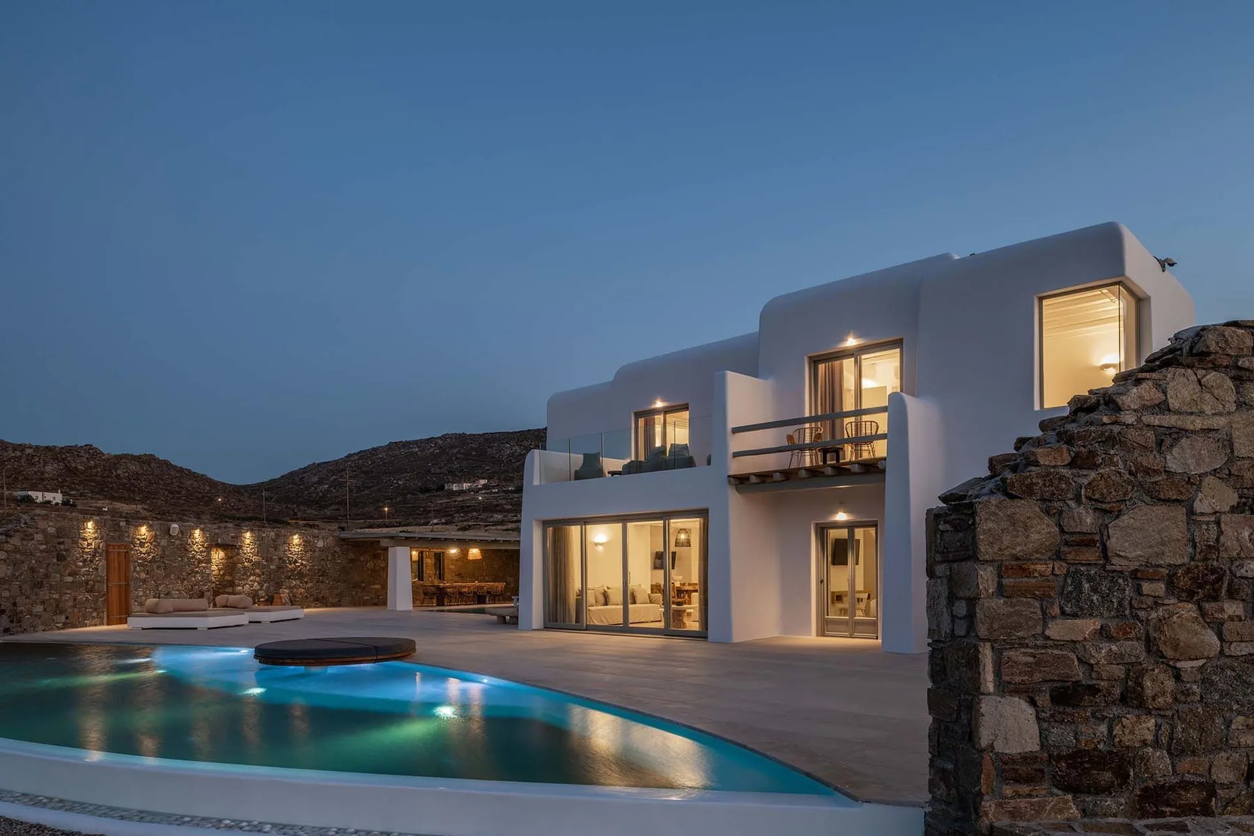 A modern white house overlooks a lit swimming pool at dusk.