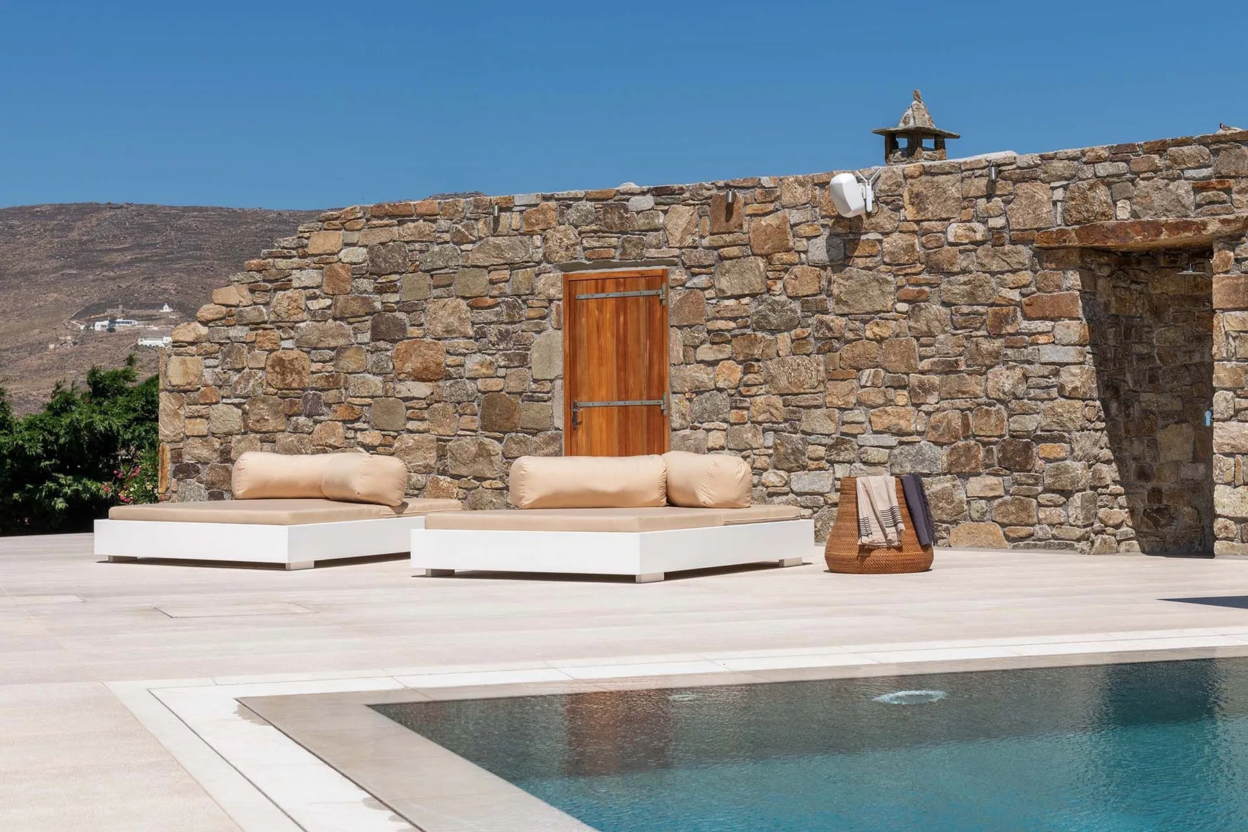A poolside terrace with cushioned loungers beside a stone wall.