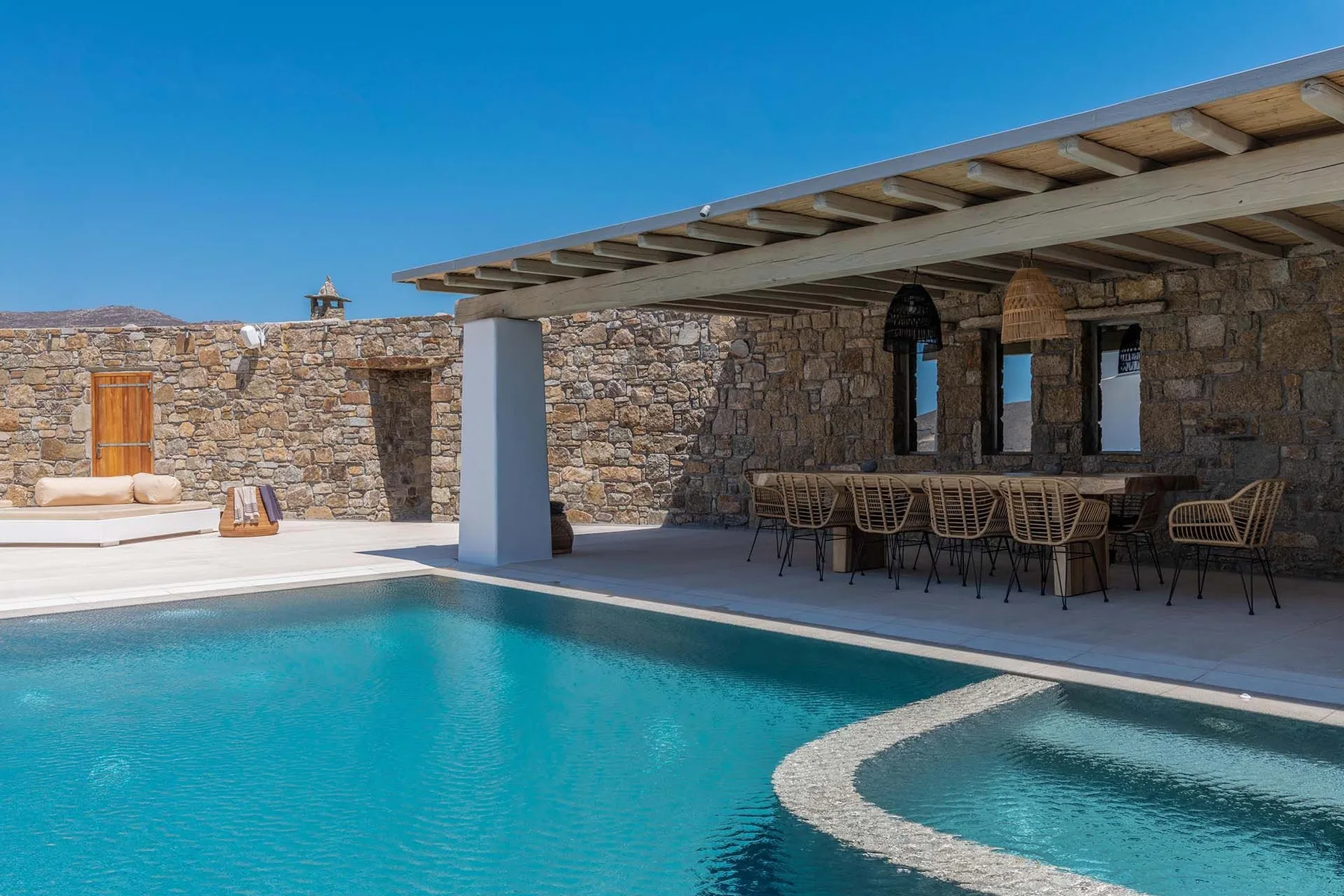 A swimming pool beside a shaded stone patio with outdoor seating.