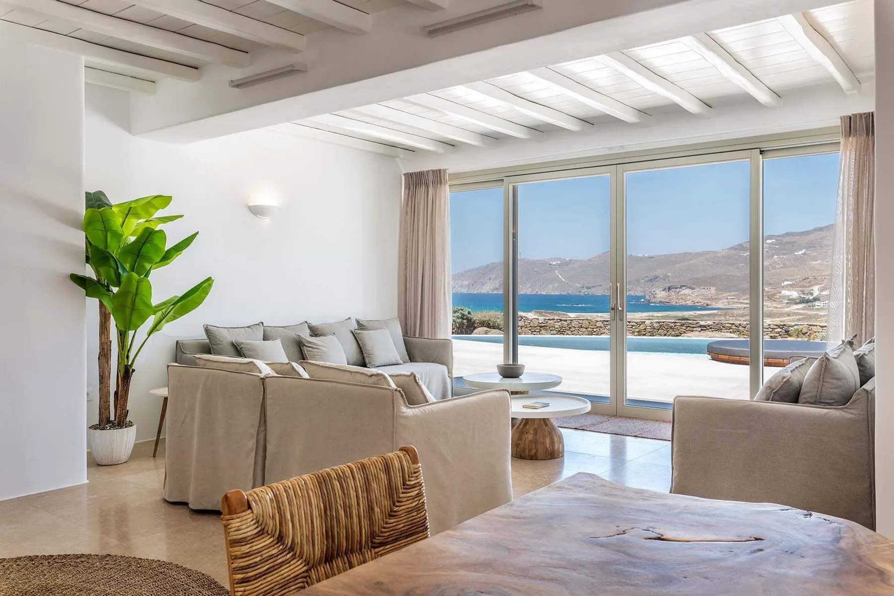A bright living room with seating beside large windows overlooking the sea.