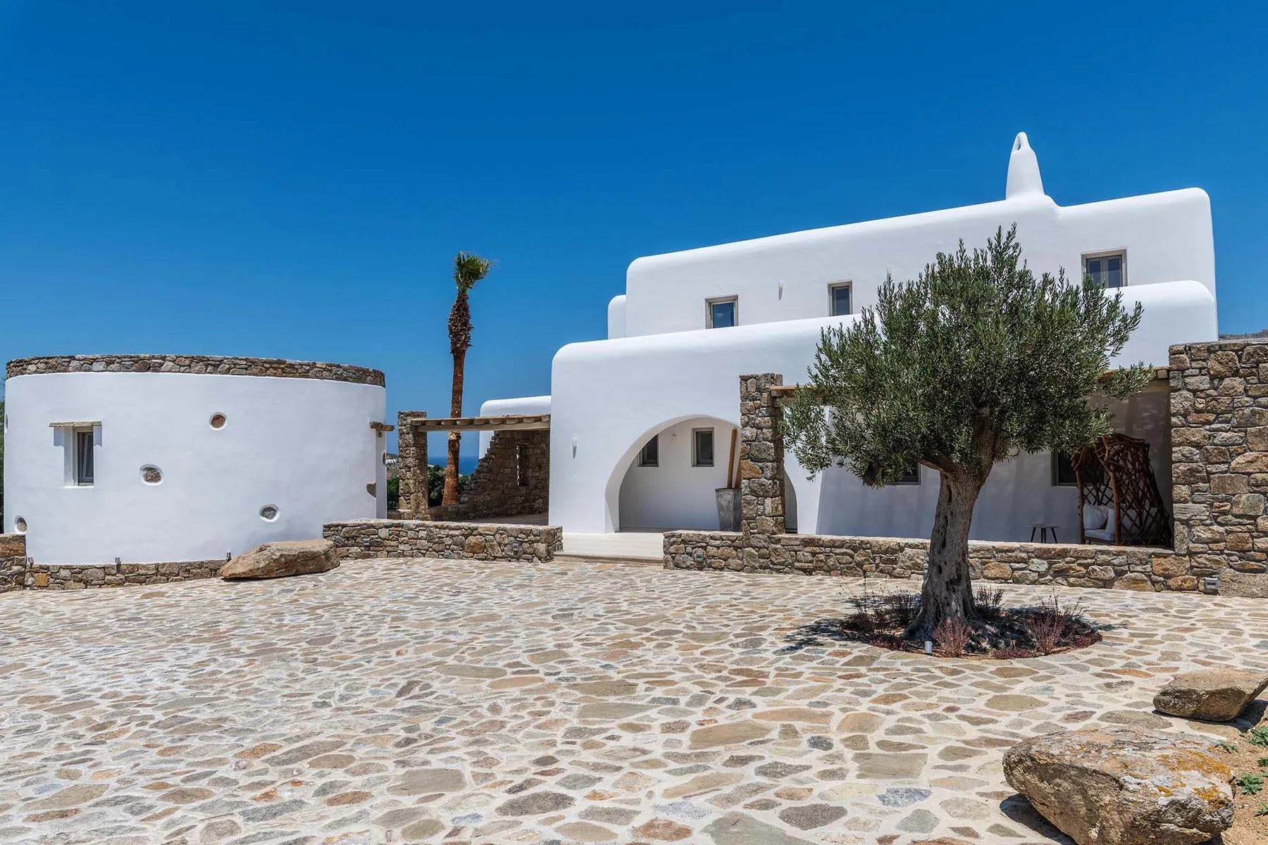 White buildings frame a stone-paved courtyard with a tree.