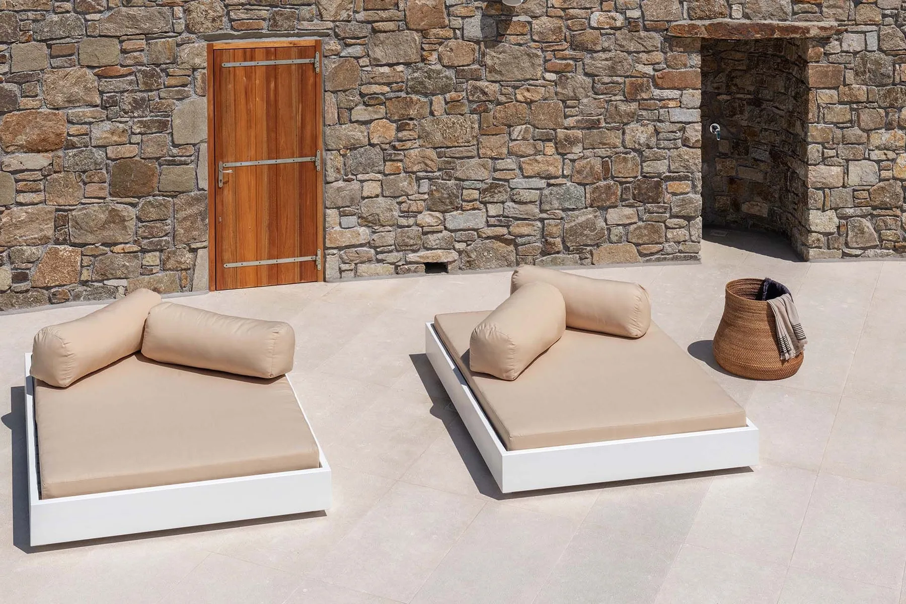 A stone-walled patio has two low cushioned loungers and a woven basket.