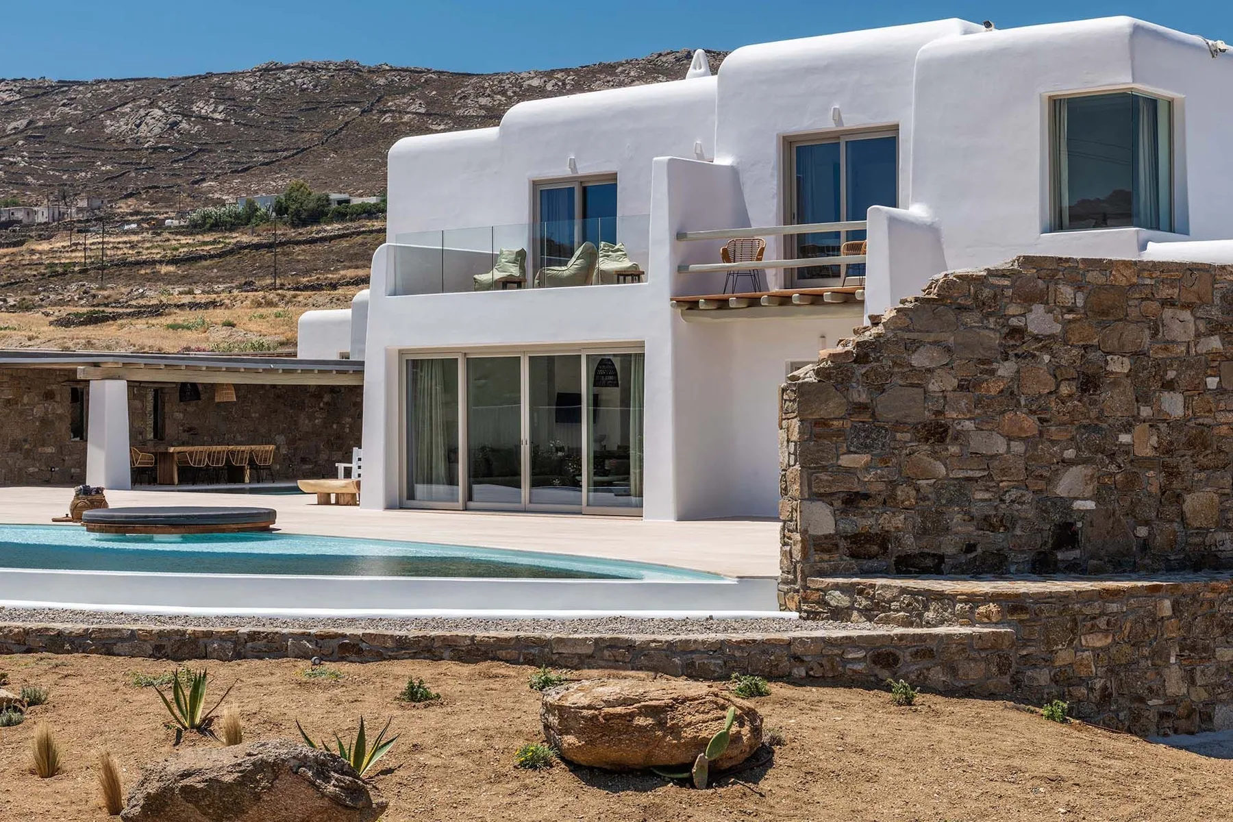 A white modern house overlooks a swimming pool and dry, rocky terrain.