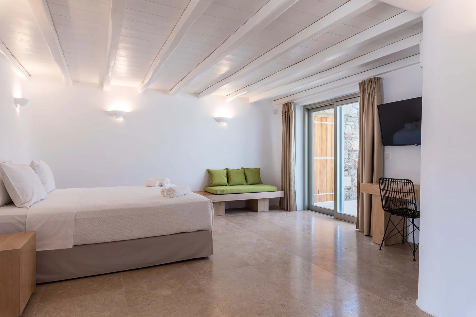 A bright bedroom with a bed, a small green sofa, and sliding glass doors.