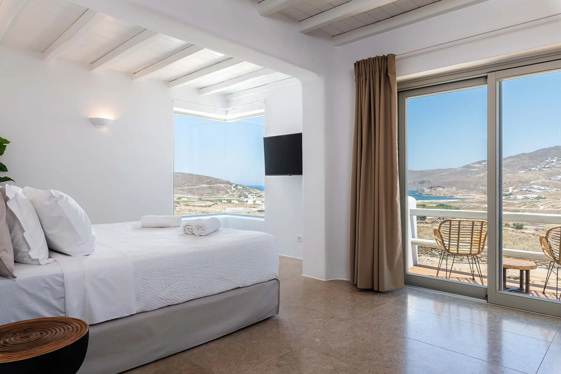 A bright bedroom with a neatly made bed and sliding glass doors overlooking the landscape.