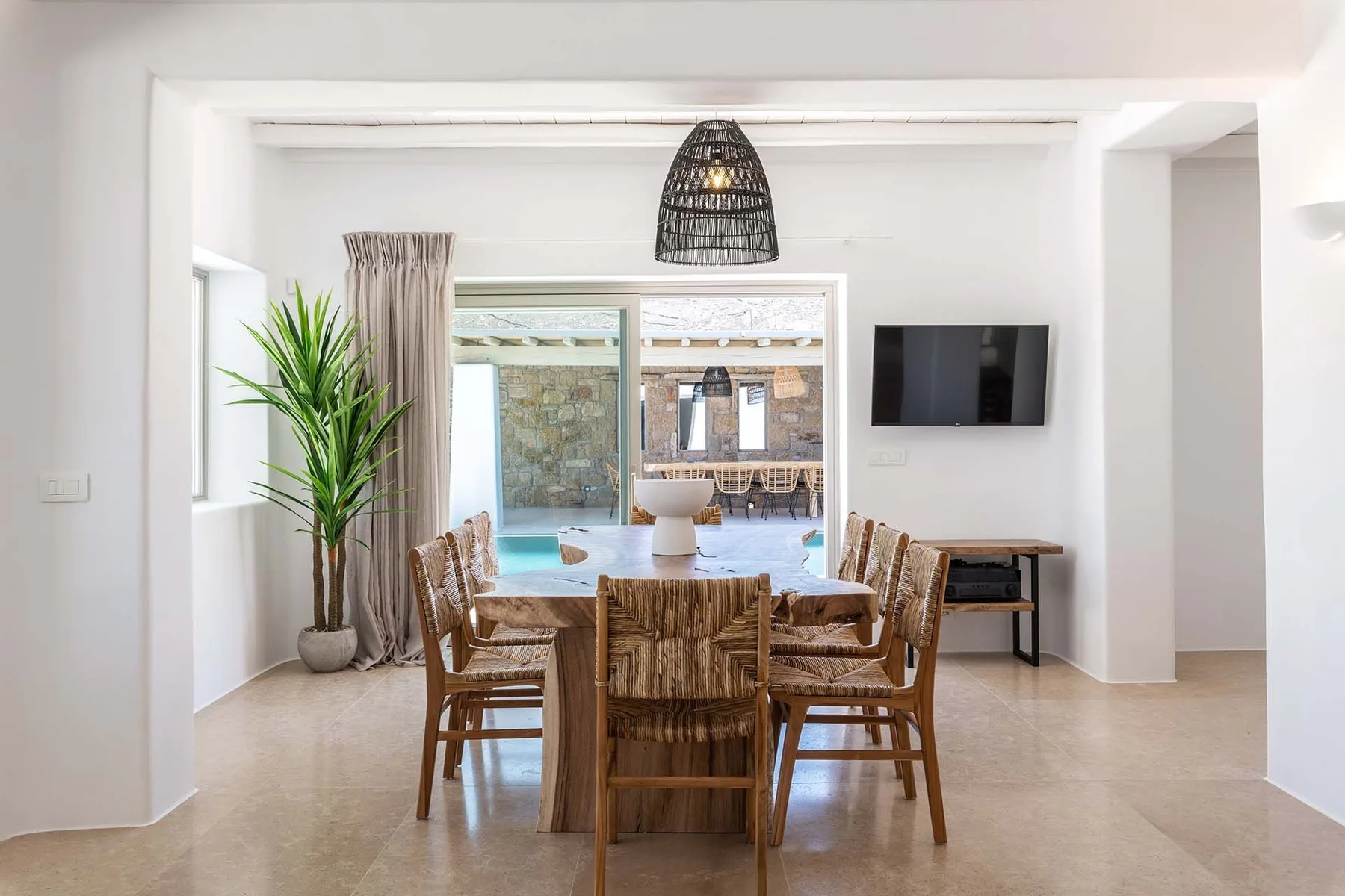 A dining area with wooden seating and a view through glass doors to a pool.