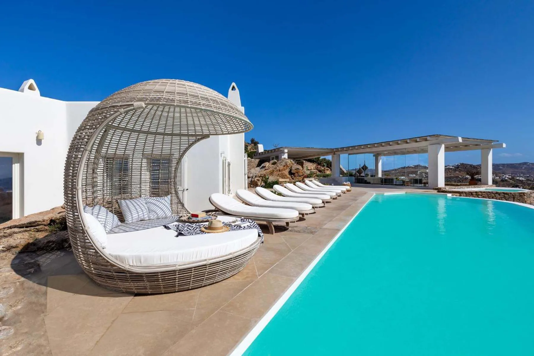 A sunny pool terrace features turquoise water and curved outdoor seating.
