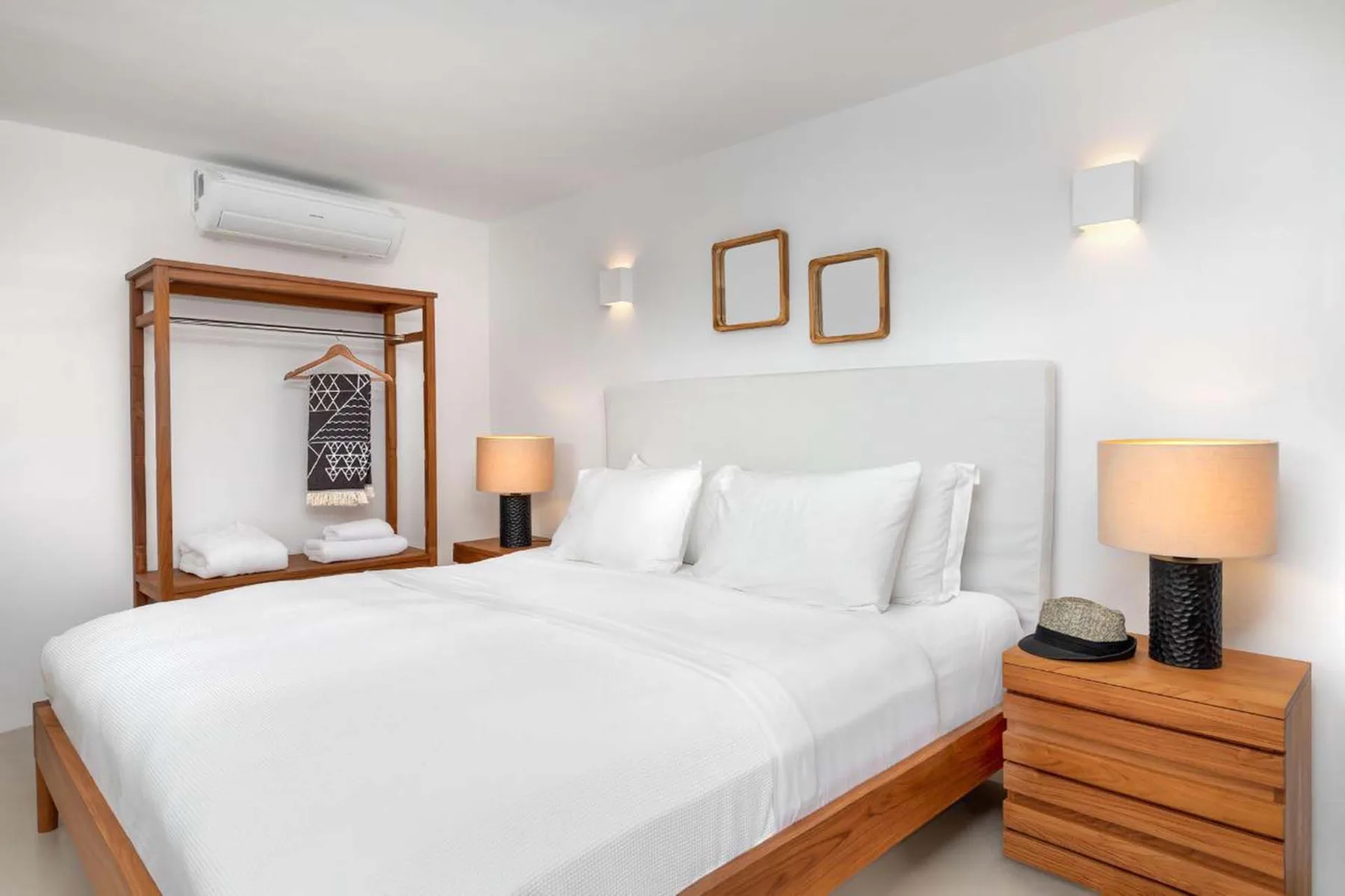 A bright bedroom with a white bed and a wooden clothing rack.