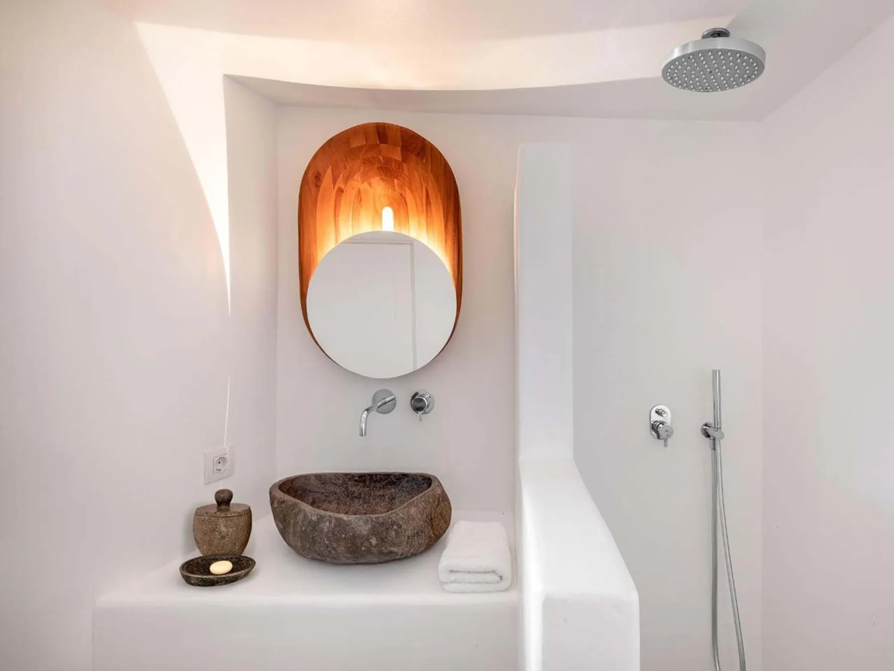 A bathroom vanity with a stone basin, round mirror, and wall-mounted shower fixtures.