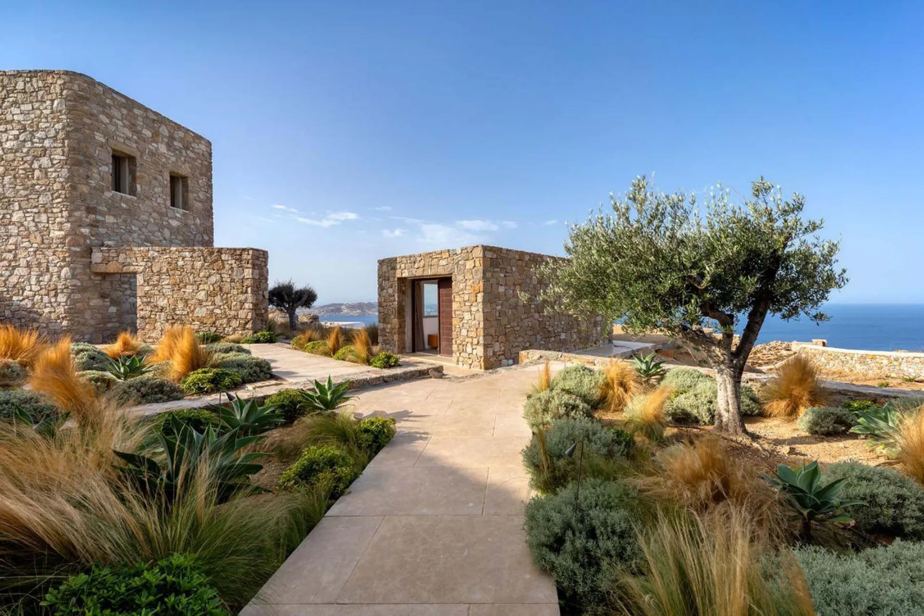 A stone building and walkway sit among landscaped plants beside the sea.