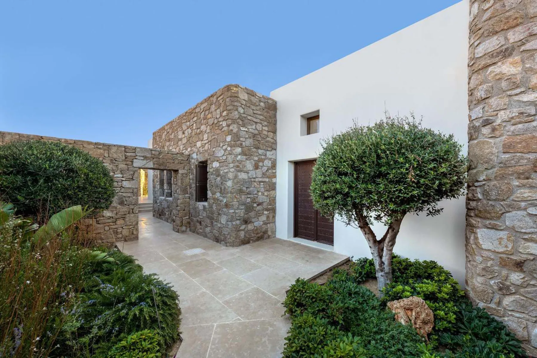 A stone courtyard path leads to a white exterior wall and dark doorway.