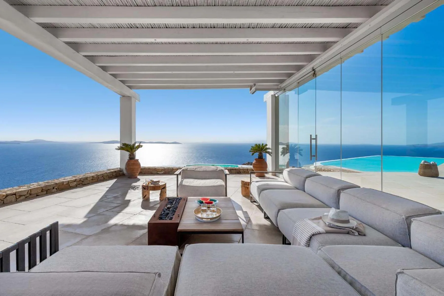 A covered outdoor lounge opens onto a sea view, with cushioned seating and a low table.