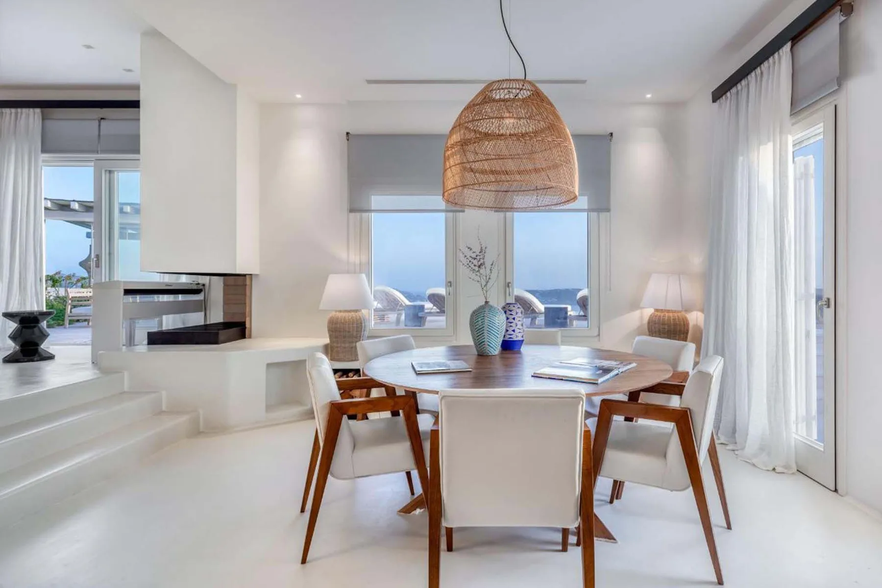 A bright dining area with a round table and large windows overlooking the water.