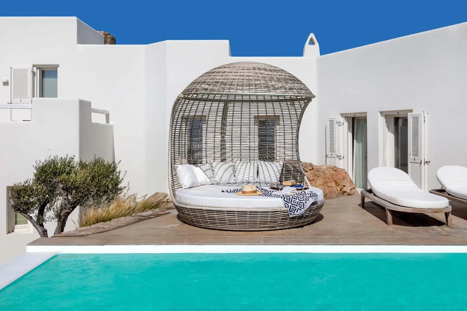 A poolside patio with a curved wicker daybed and white loungers.