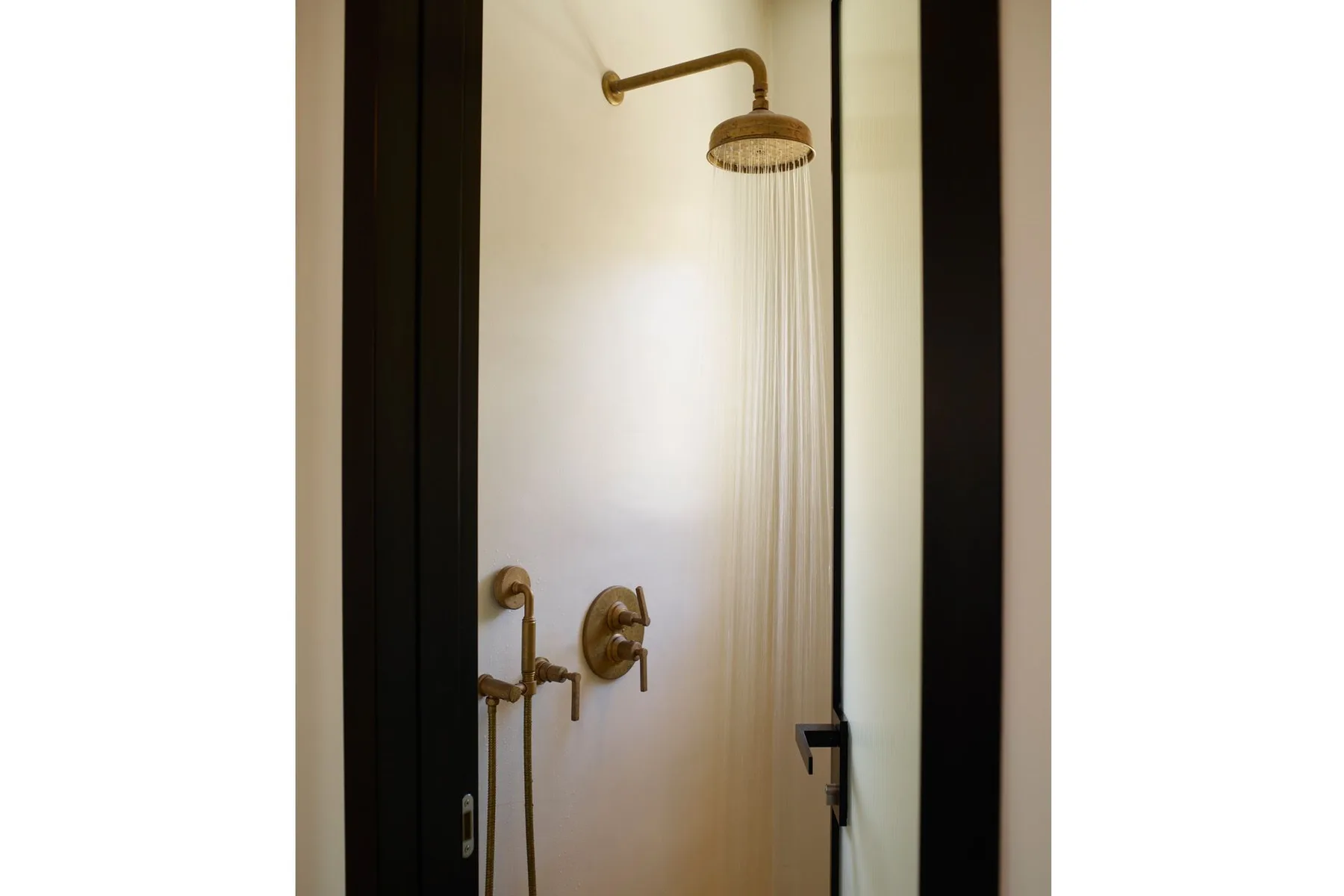 A shower with brass-colored fixtures and water flowing from the overhead showerhead.