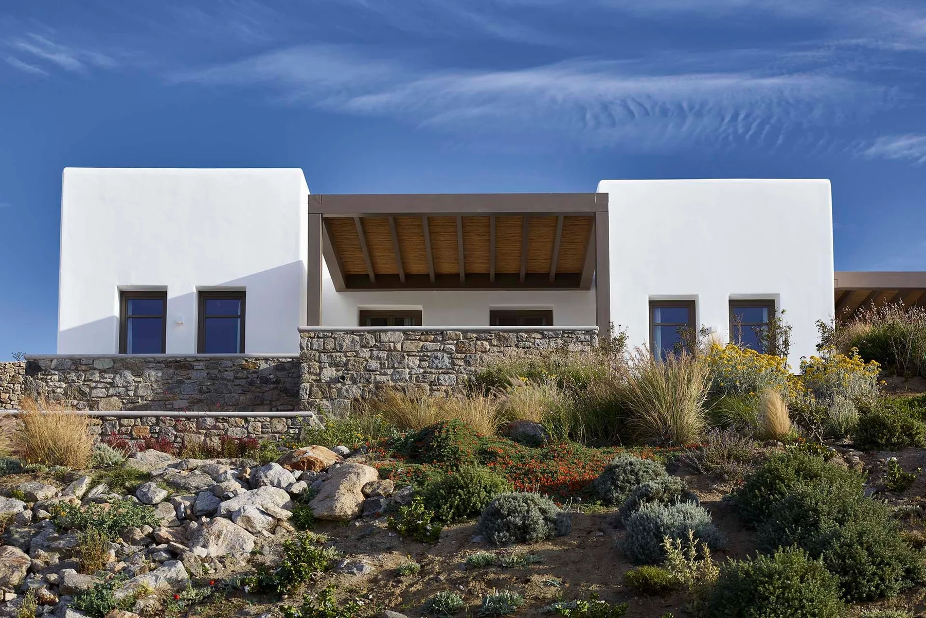 A modern white building stands behind a rocky, planted garden.