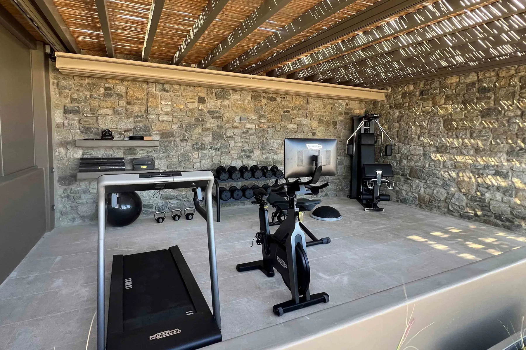 Shared amenity: A gym with exercise equipment and a treadmill under a slatted roof.