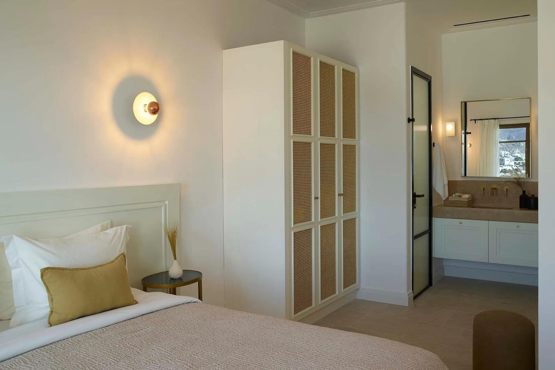 A bedroom with a bed beside a tall cabinet and an open bathroom doorway.