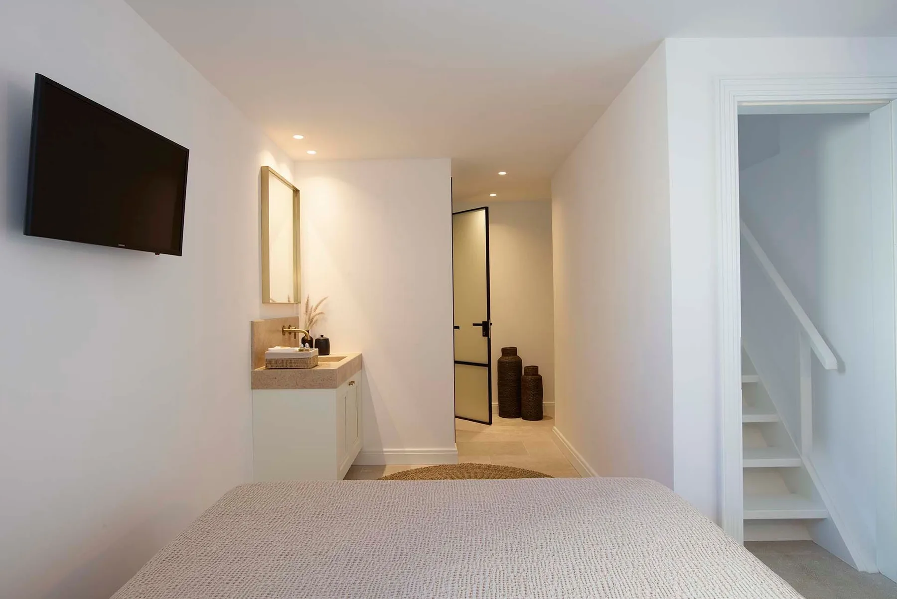 A bedroom with a bed, wall-mounted television, and a vanity along the wall.