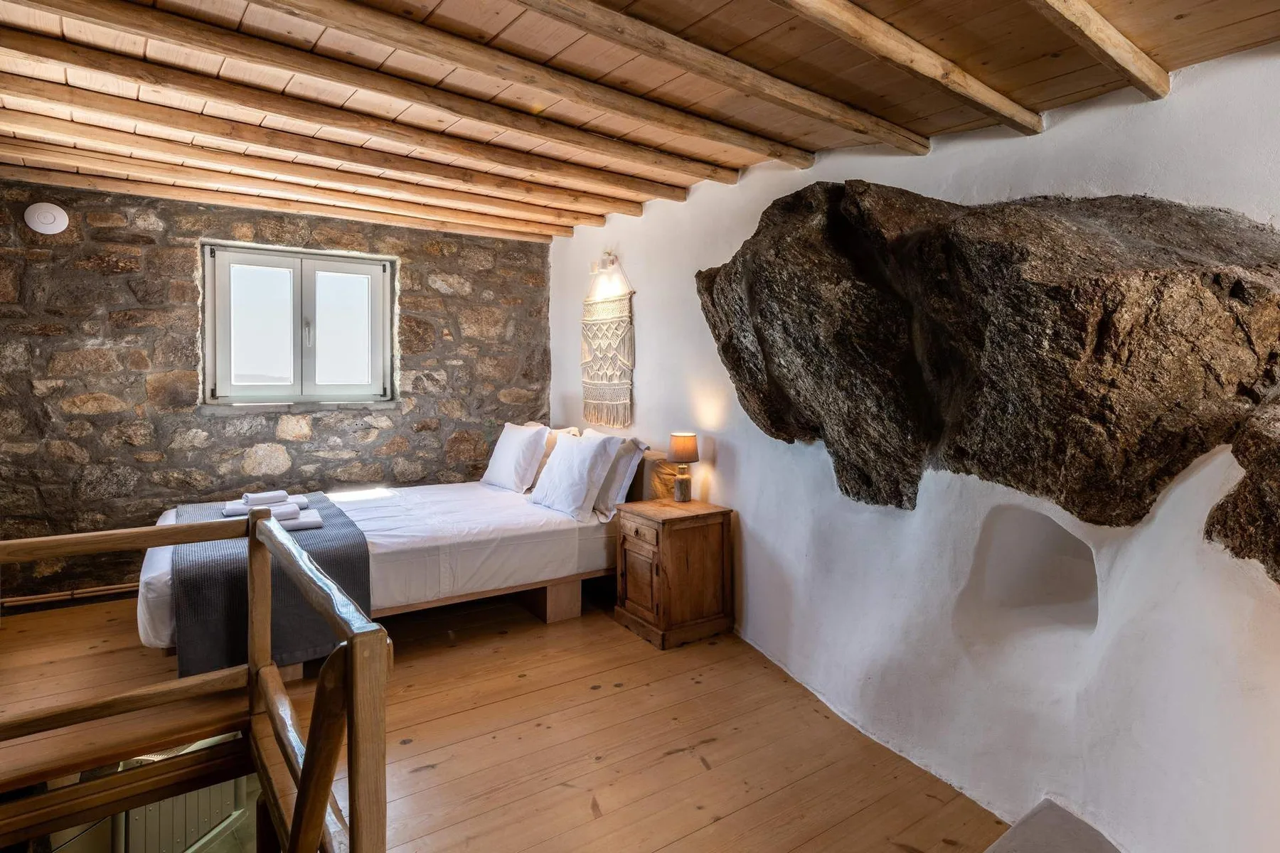 A rustic bedroom with a wooden bed beside an exposed stone wall.