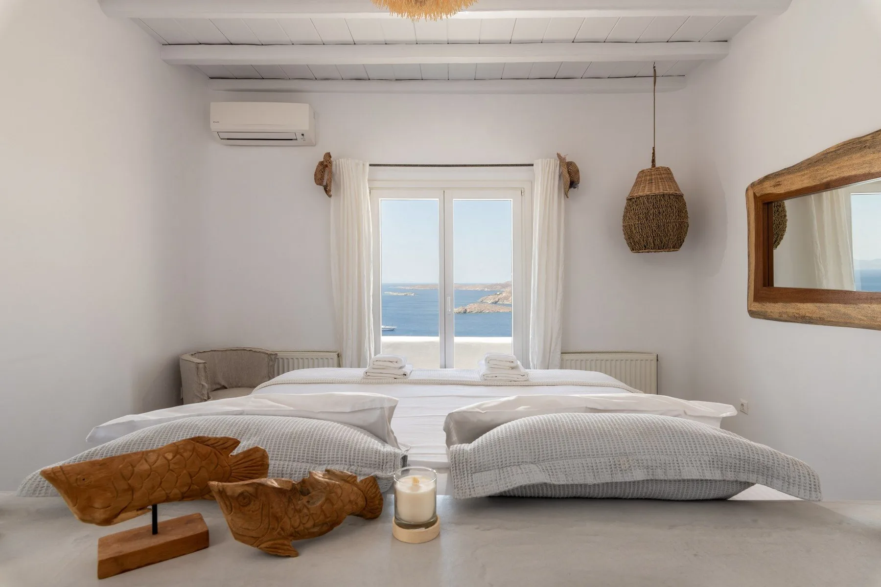 A bright bedroom with a low bed and a sea view through the window.